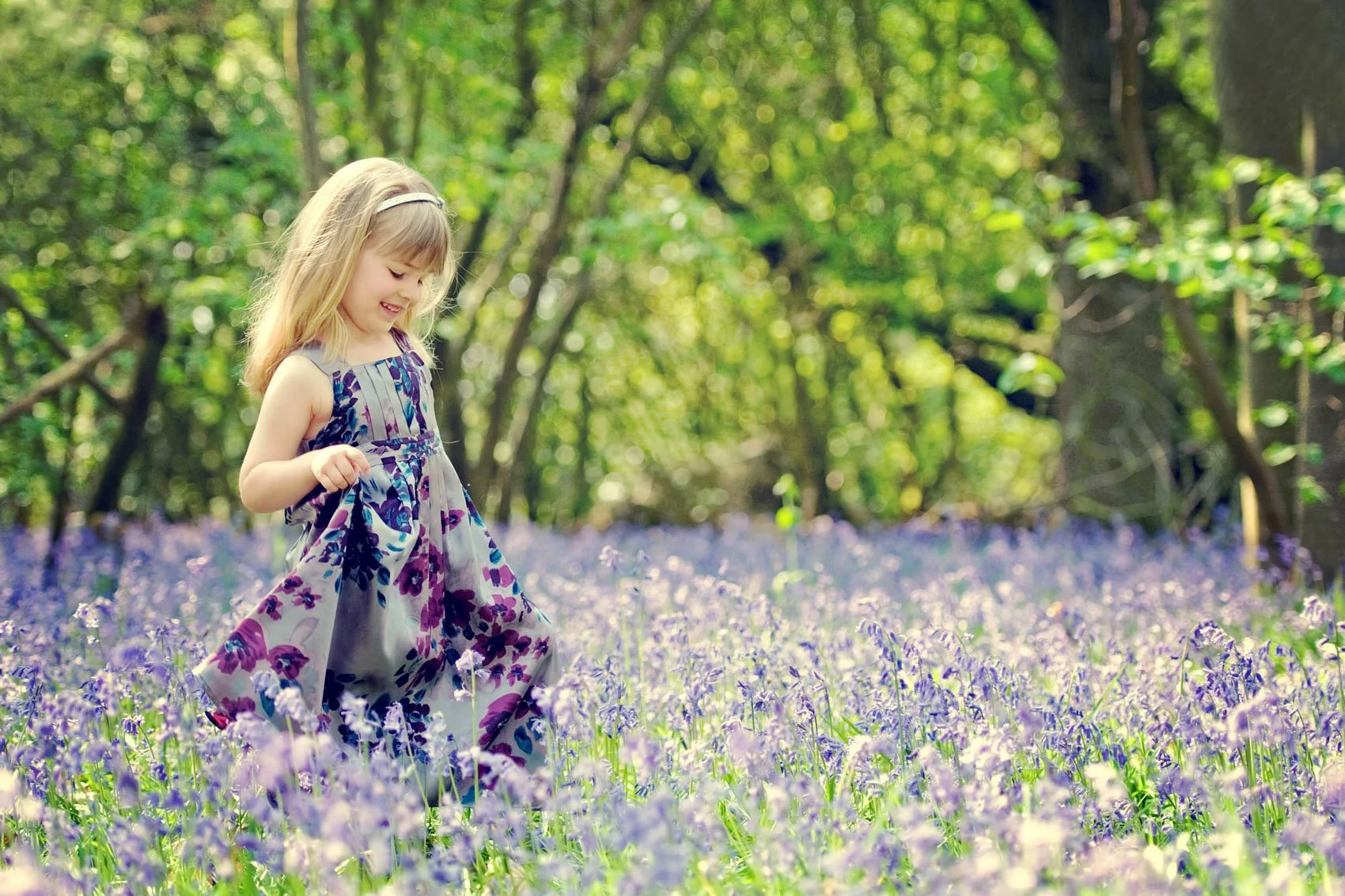 A little girl holds up the hem of her dress and smiles as she walks through bluebells in Highgate Wood in north London 