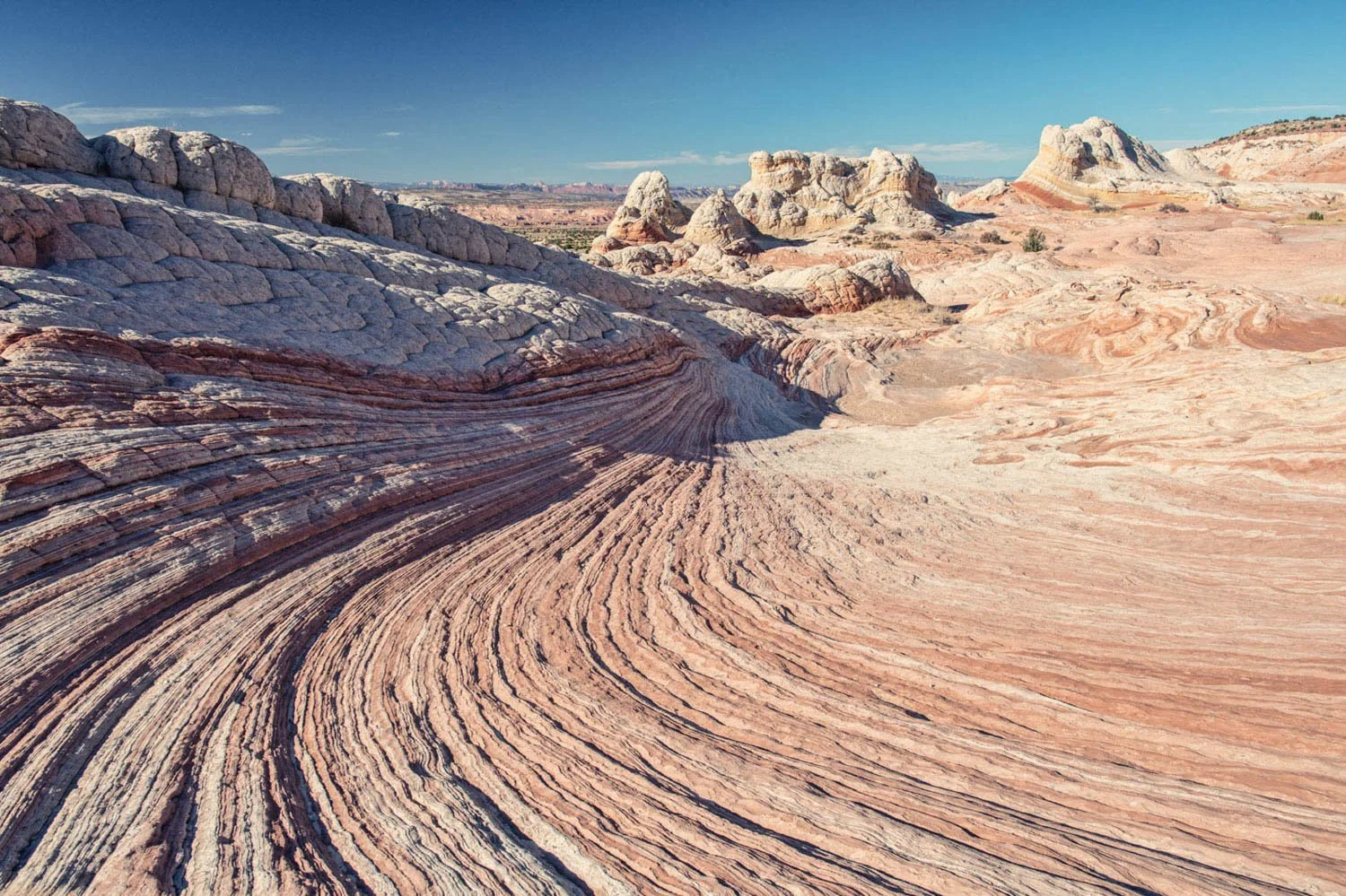 Rock formations  in Utah with layered stripes in a desert landscape under a blue sky.