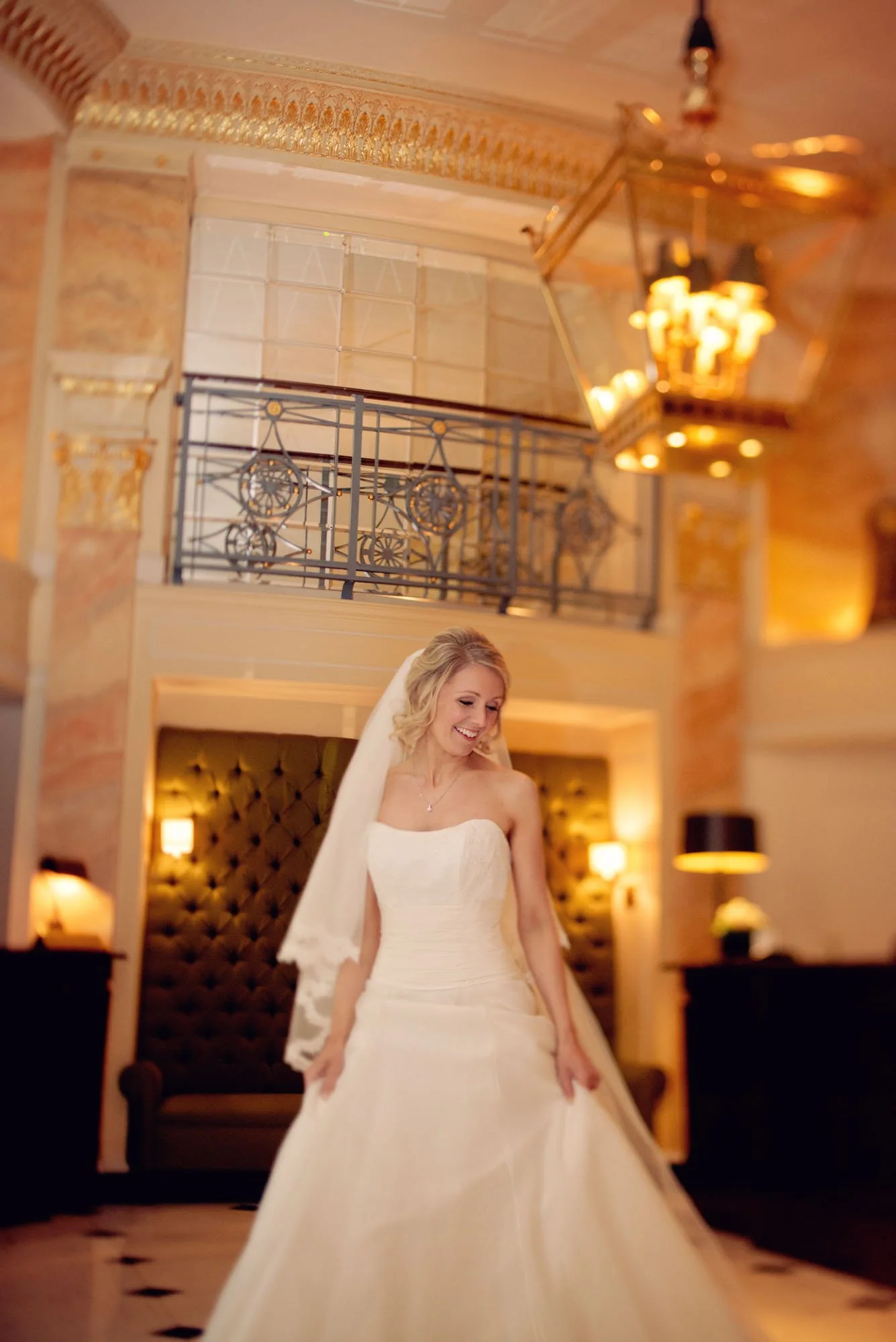 A bride holds her dress and smiles down as she stands in the foyer during her micro wedding at the Dorchester Hotel in London 