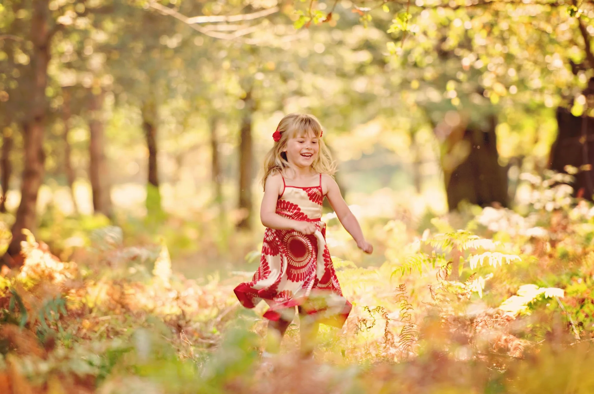 Happy little girl runs through the ferns in the woods at Hampstead Heath flooded with golden late afternoon light