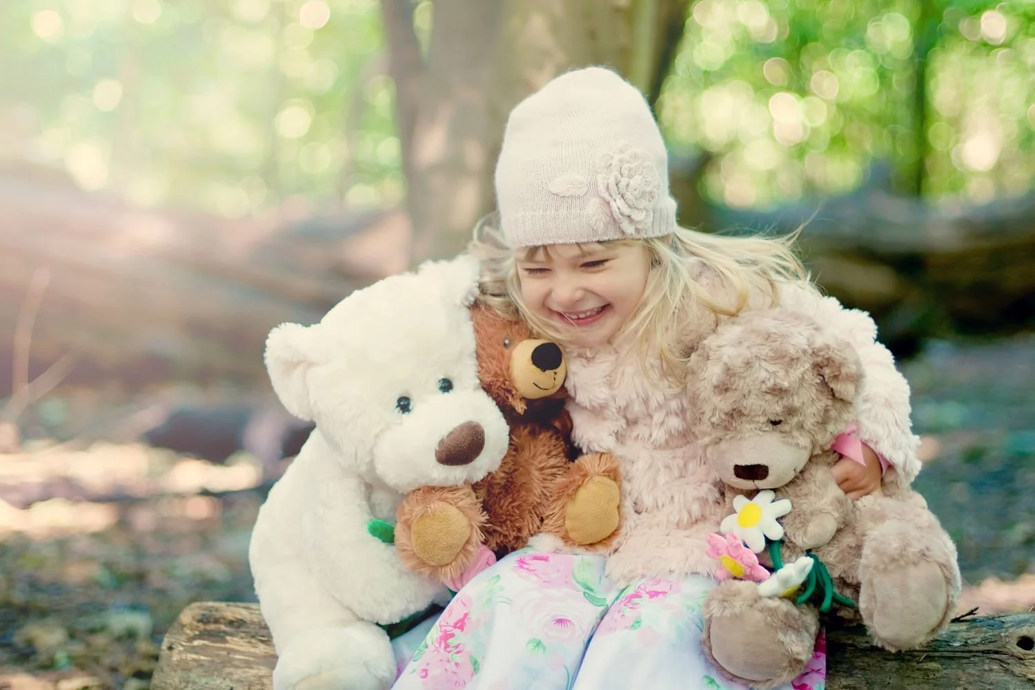 Little girl hugs her toys and smiles in delight during a family photoshoot in Hampstead Heath, with dappled sunlight coming through the trees behind her