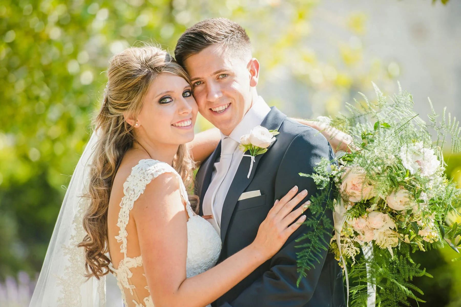 A bride and groom hold each other and smile at the camera while the bride holds her bouquet, during their spring wedding at Kenwood House in Hampstead Heath in north London 