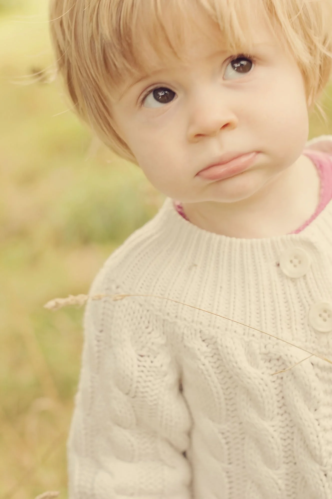 Little girl pouts mischievously up at the camera during a family photoshoot in Hyde Park in London