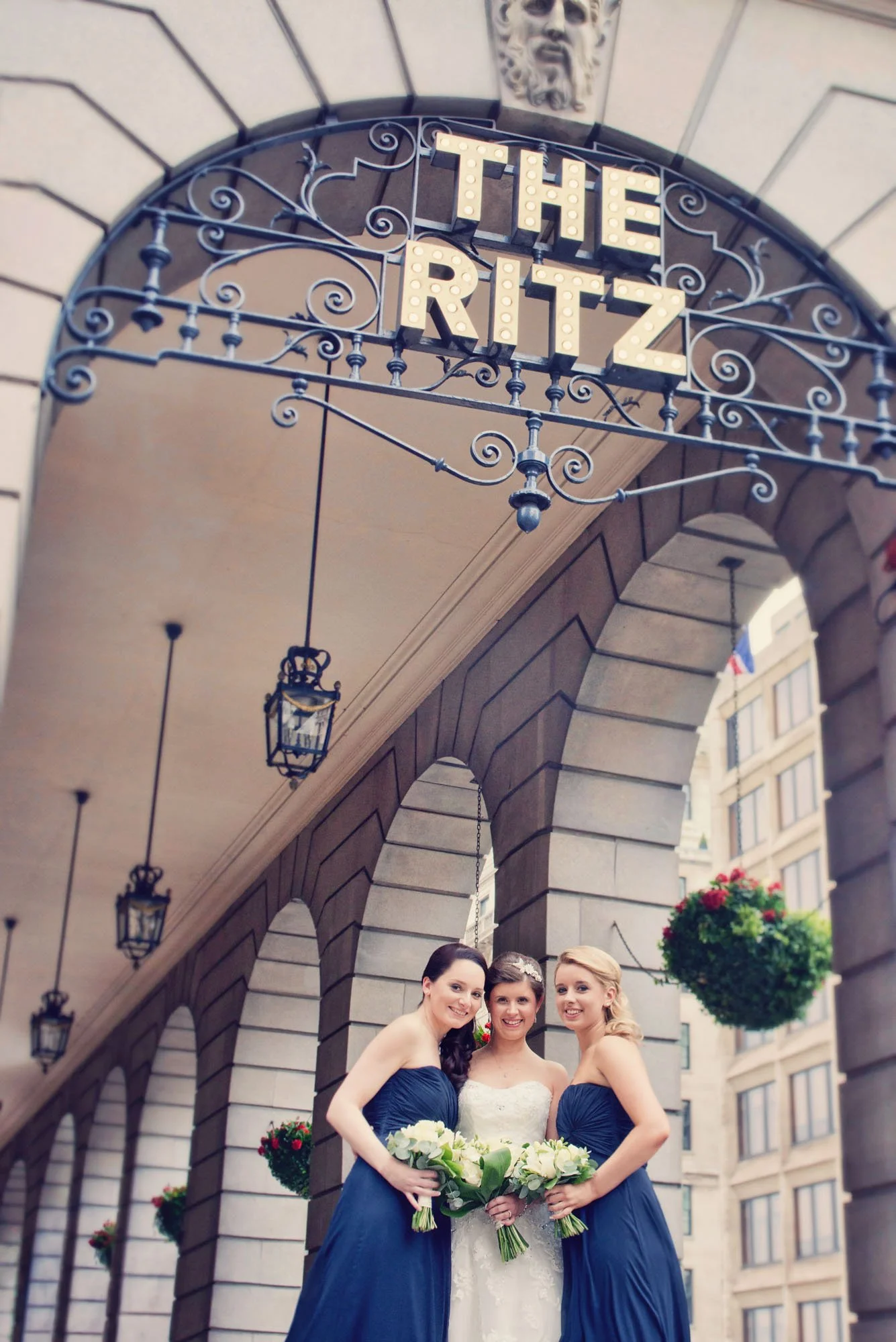 A bride stands with her two bridesmaids underneath the famous Ritz sign during her micro wedding at The Ritz hotel in London