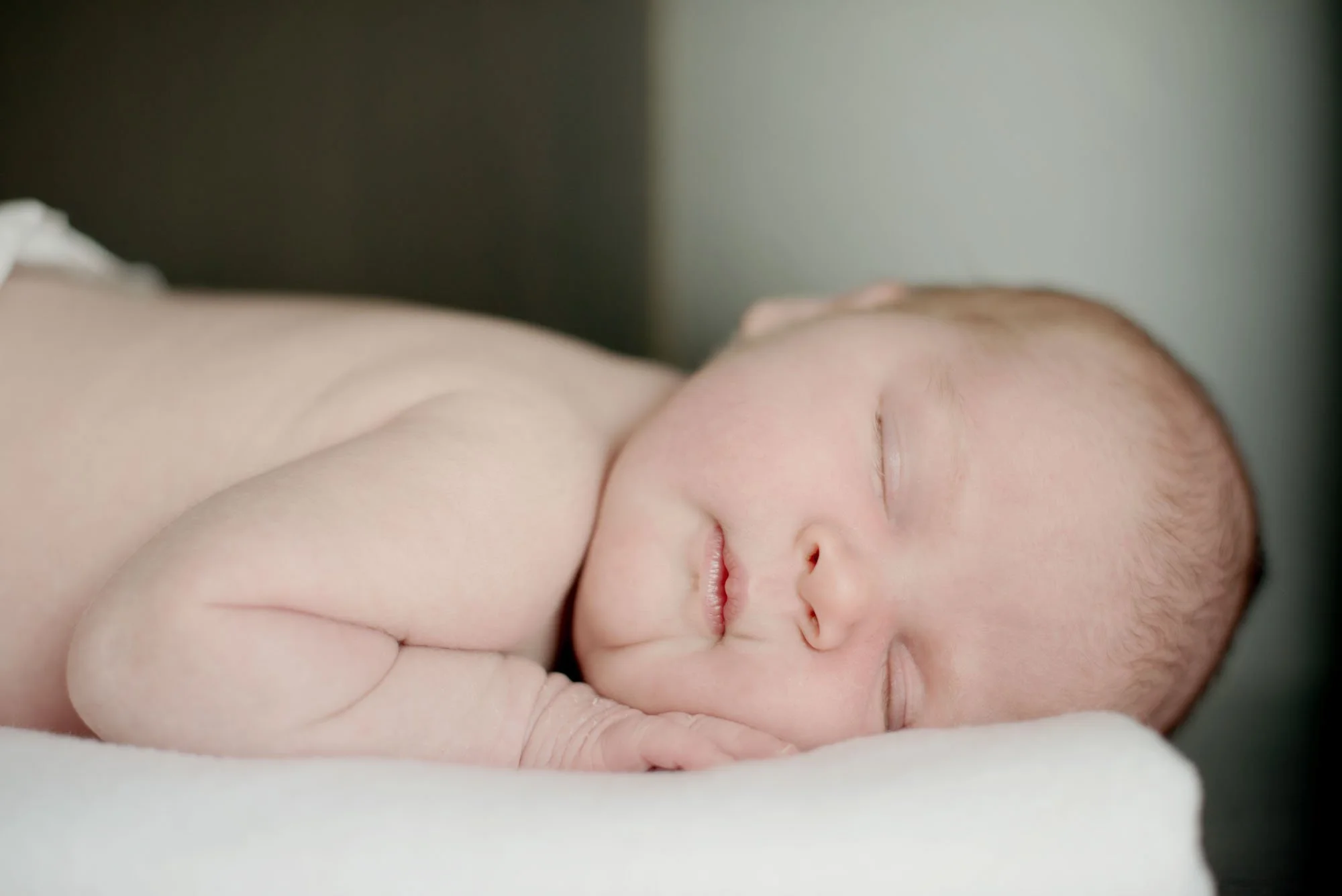 A newborn baby sleeps peacefully during a newborn photoshoot in Islington in London.  She lies on her front with her cheek resting on her hand.