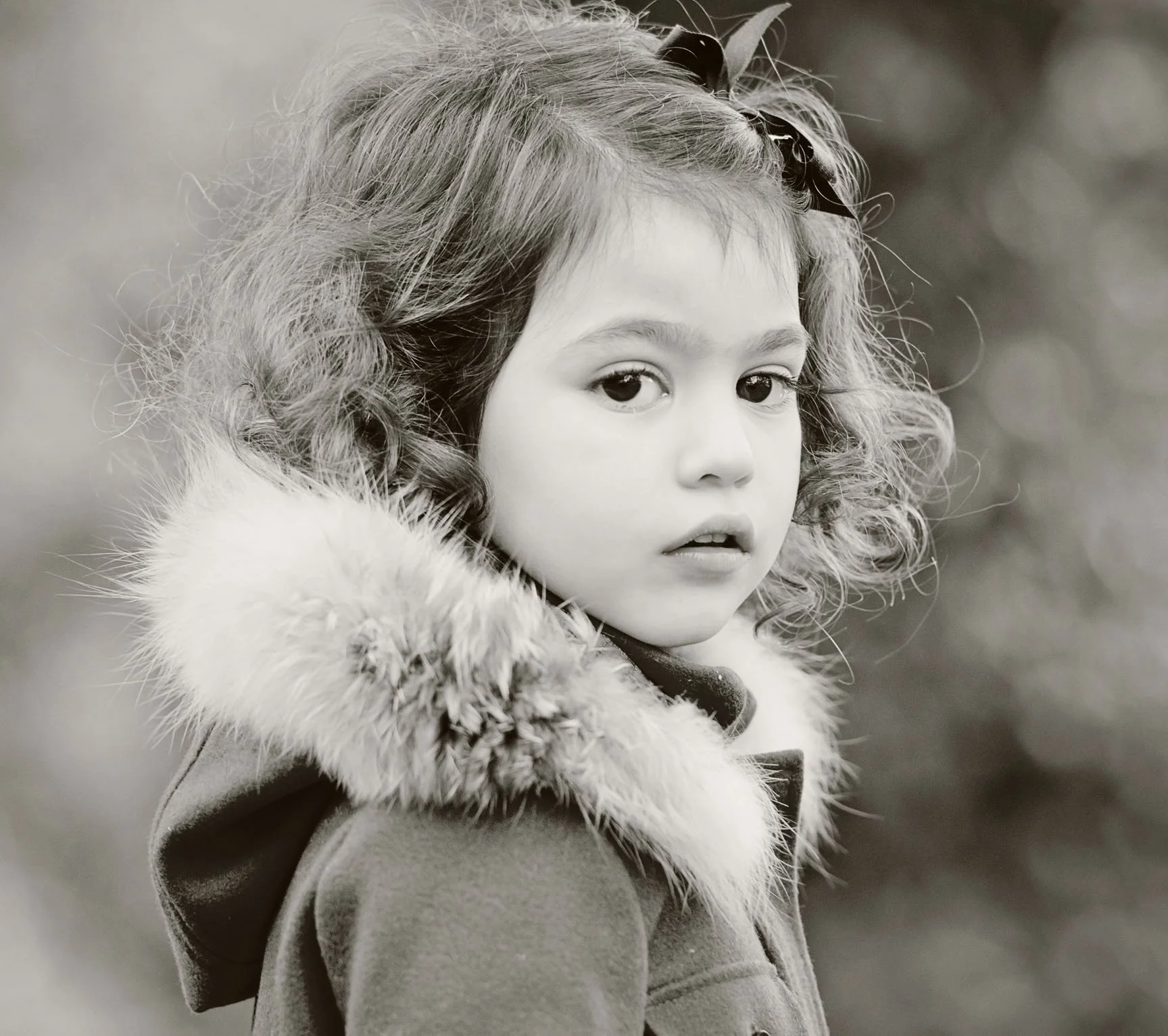 A black and white photo of a little girl with ringlets wearing a fur-trimmed hood in Regent's Park in London 