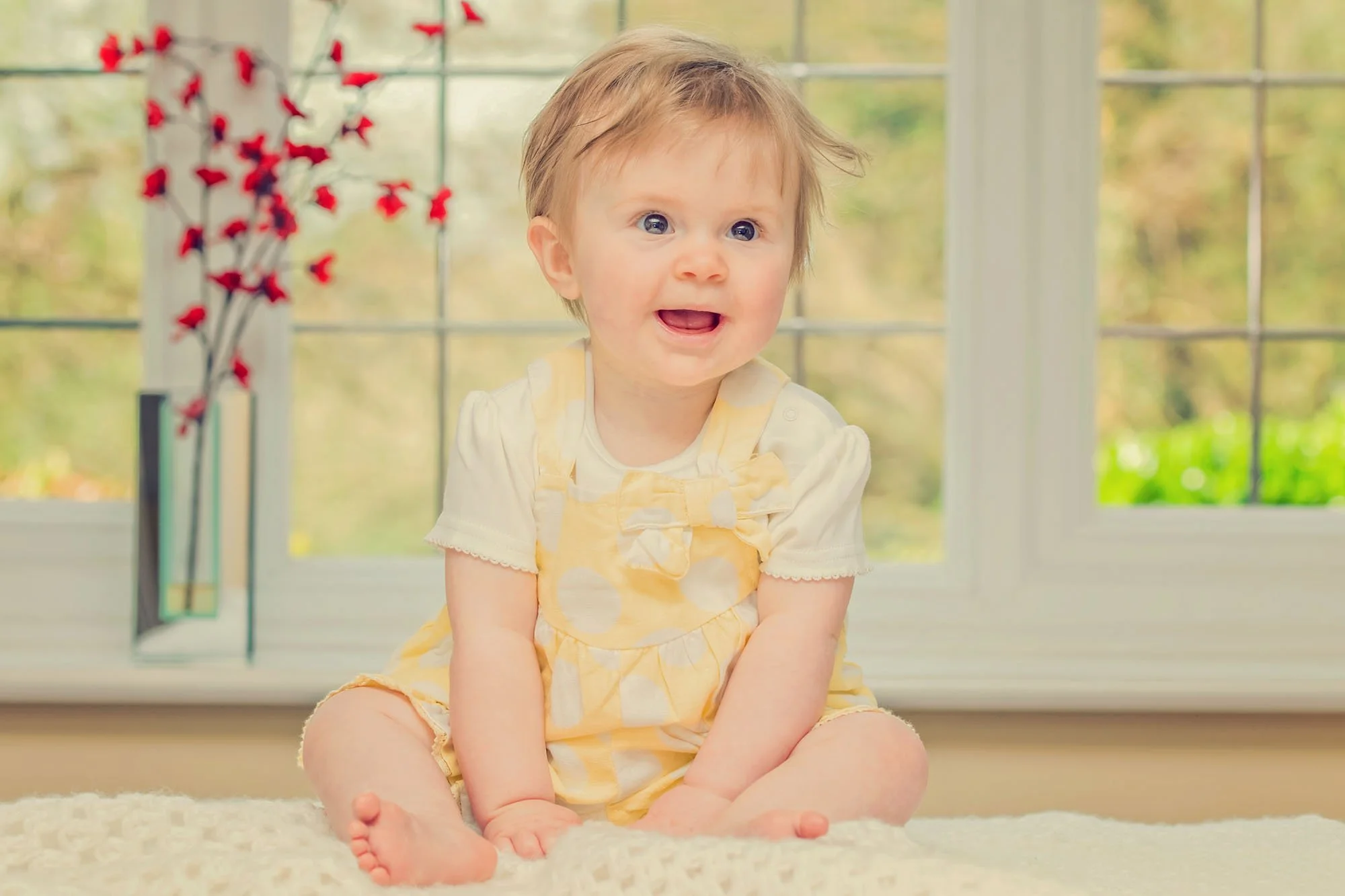 An eight month old little girl in a yellow dress sits on her kitchen counter at home in Clapham in south west London
