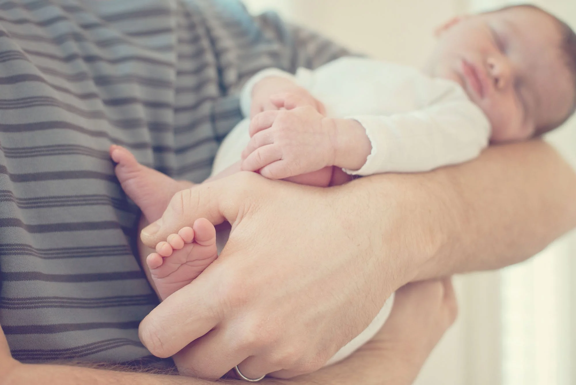 A father holds his newborn baby in his arms at home in South Kensington as the warm light floods the room