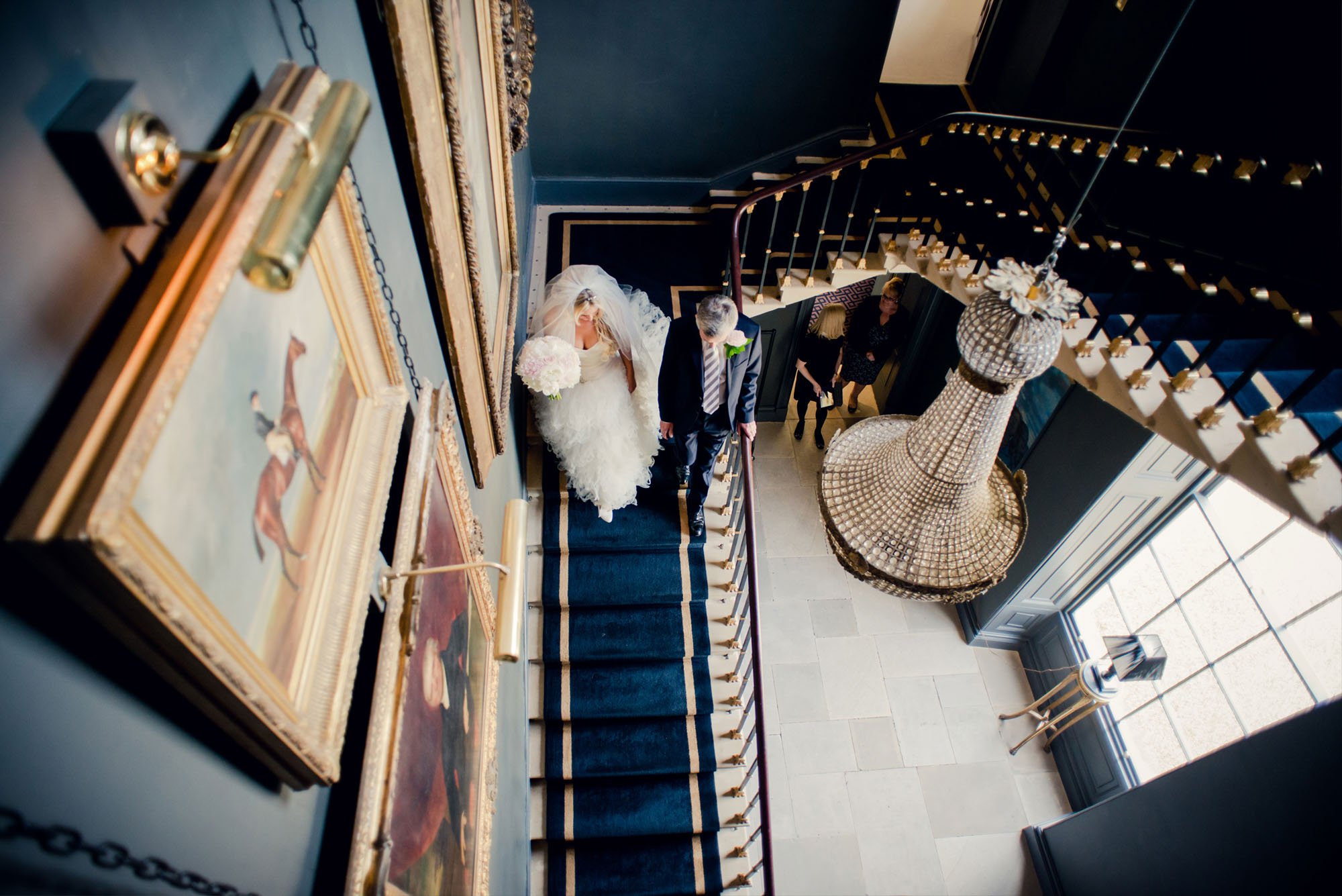 A bride walks down the stairs of a London mansion accompanied by her father.