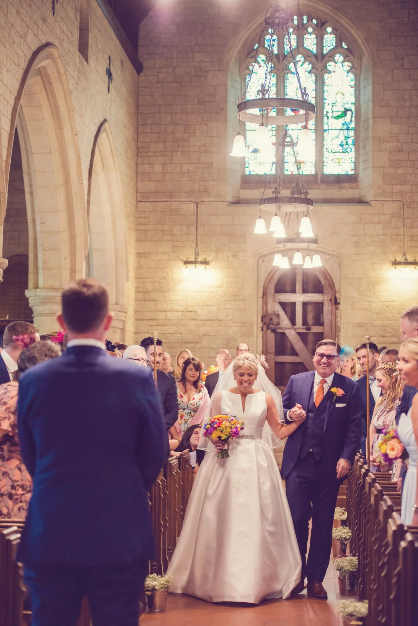 A bride grins at her husband-to-be as she walks up the aisle with her father in a church in Islington in north London