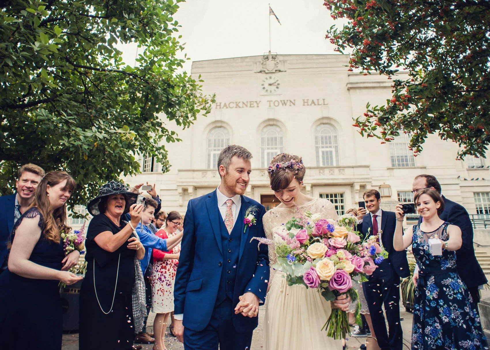 Bride and groom smiling and covered in confetti as they leave Hackney Town Hall in London after their wedding ceremony.