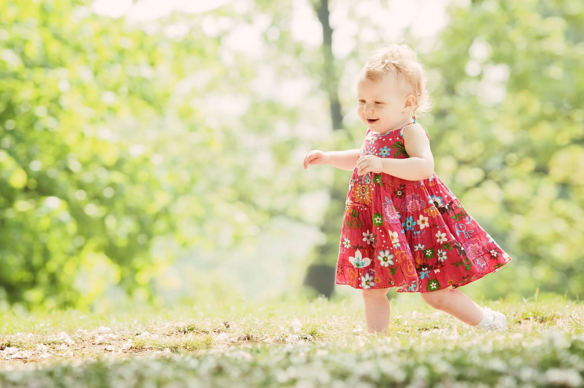 A young girl in a red floral dress running and smiling outdoors during a summer family photoshoot at Hyde Park in London