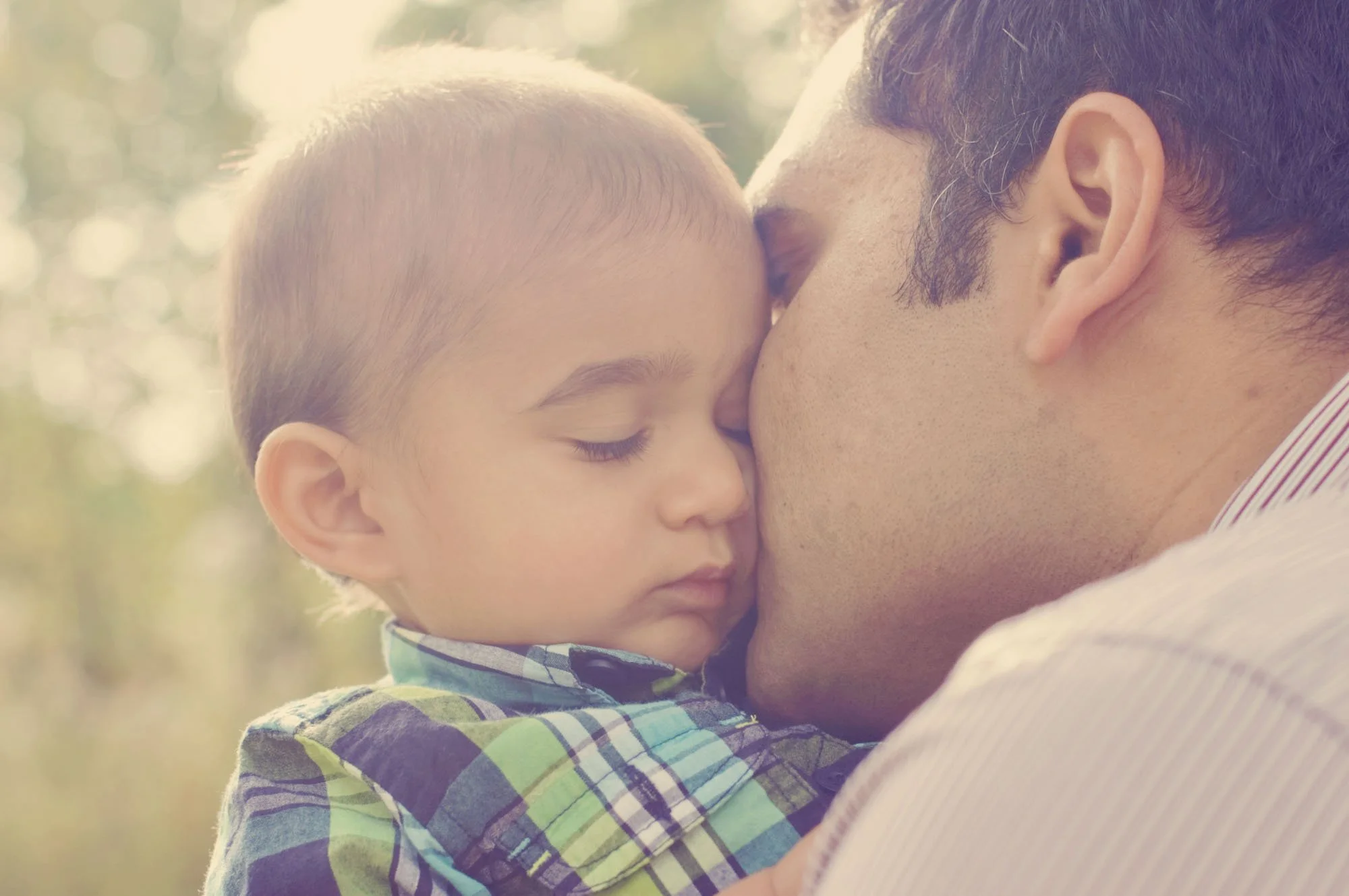 A little boy is comforted by his father's kiss during a family photoshoot in Hyde Park in London