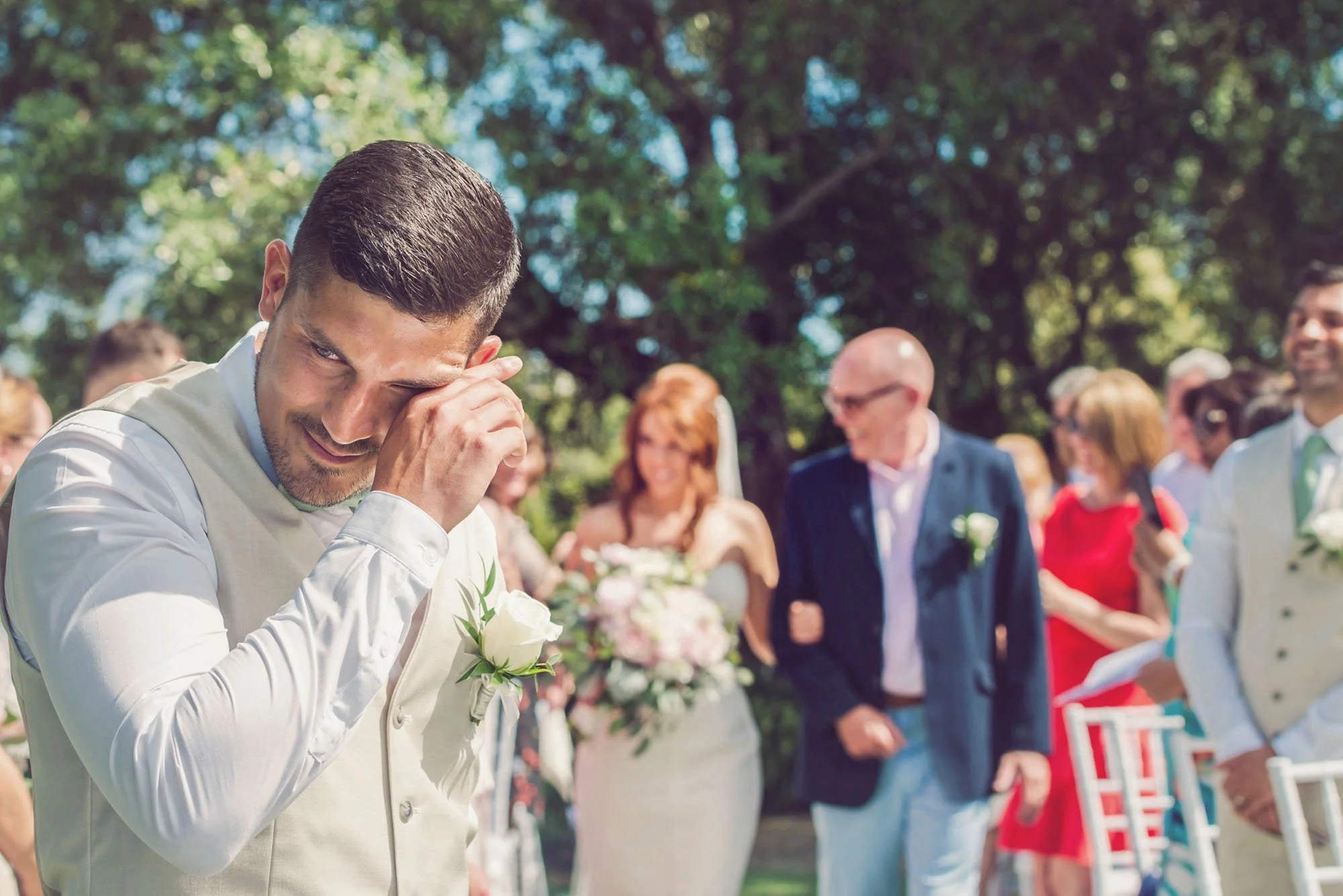 Emotional groom in outdoor wedding ceremony, as the bride walks towards him