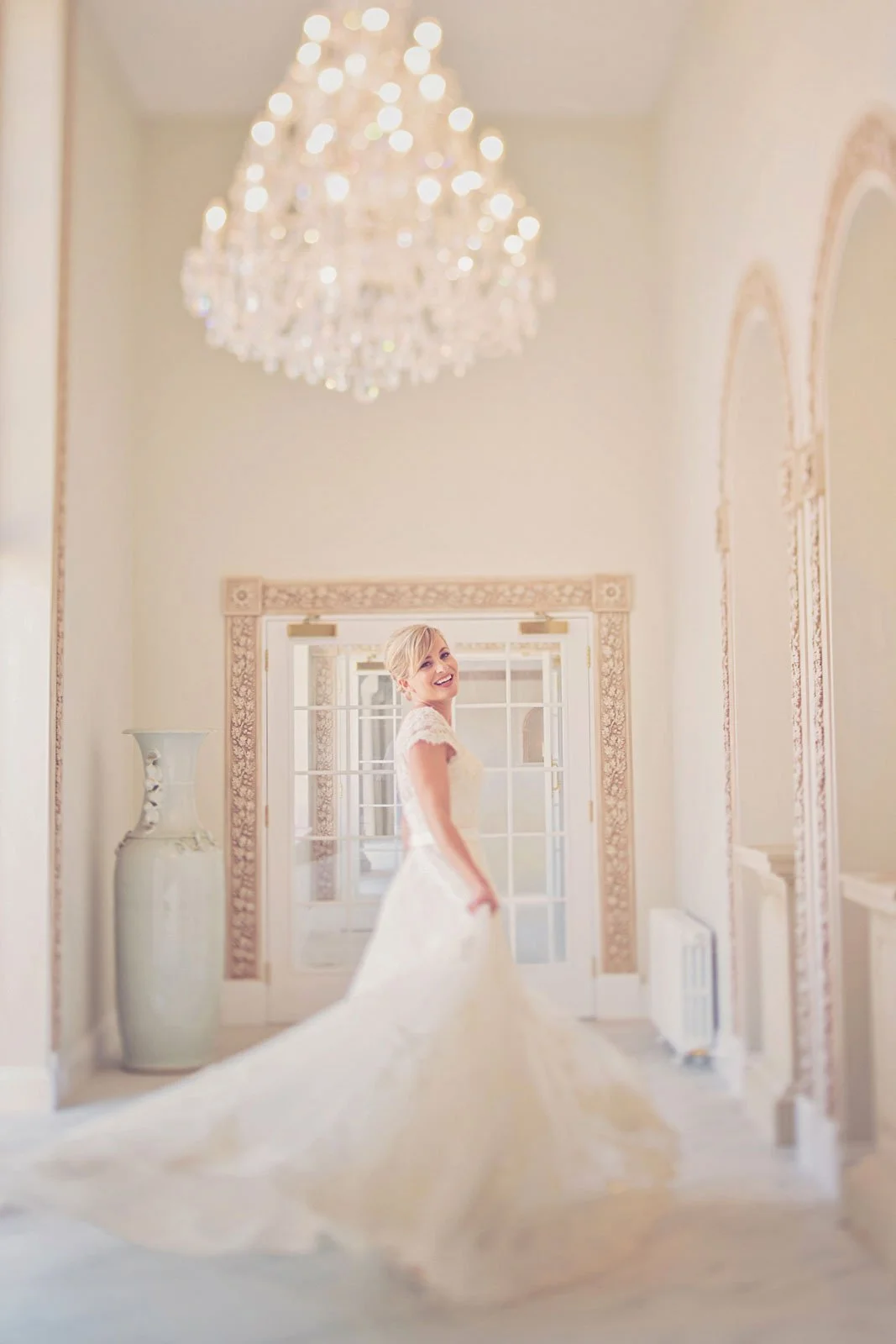 A bride laughs as she swirls her dress around under a chandelier during her wedding at Froyle Park in Hampshire