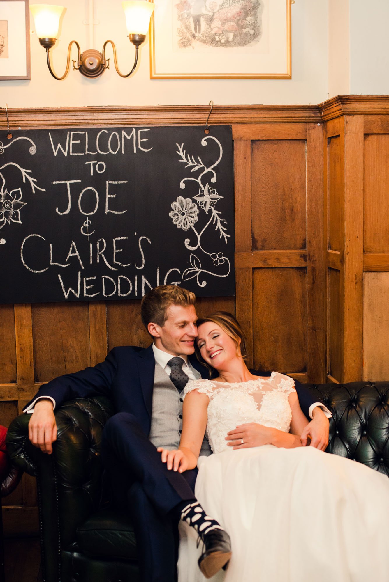 A bride leans into her groom's arms as they relax in armchairs at the Grosvenor pub, during their micro wedding in Clapham in south-west London