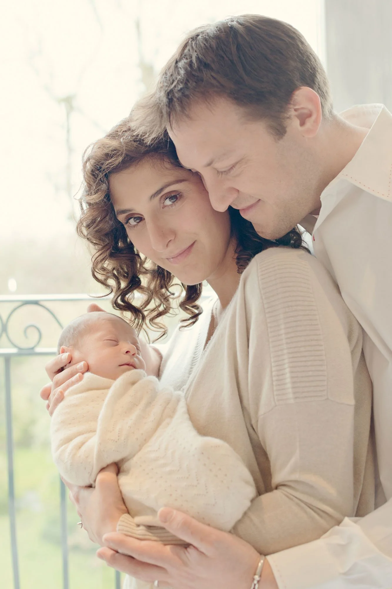 Proud new parents hold their newborn son in their arms as they stand in front of the full length window of their home in Chelsea in south west London