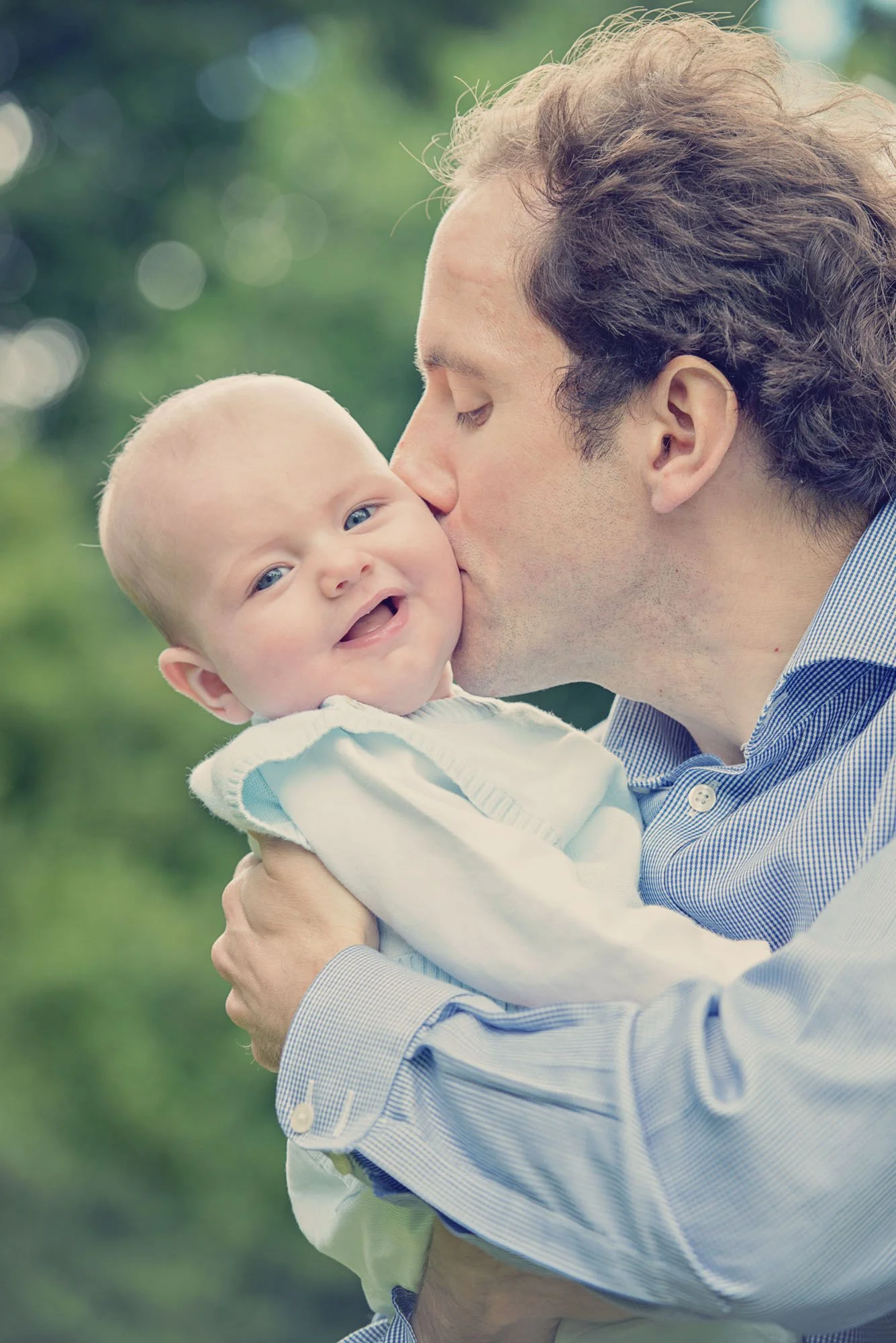A baby boy laughs as he's kissed on the cheek by his father during a family photoshoot in Richmond Park in south west London