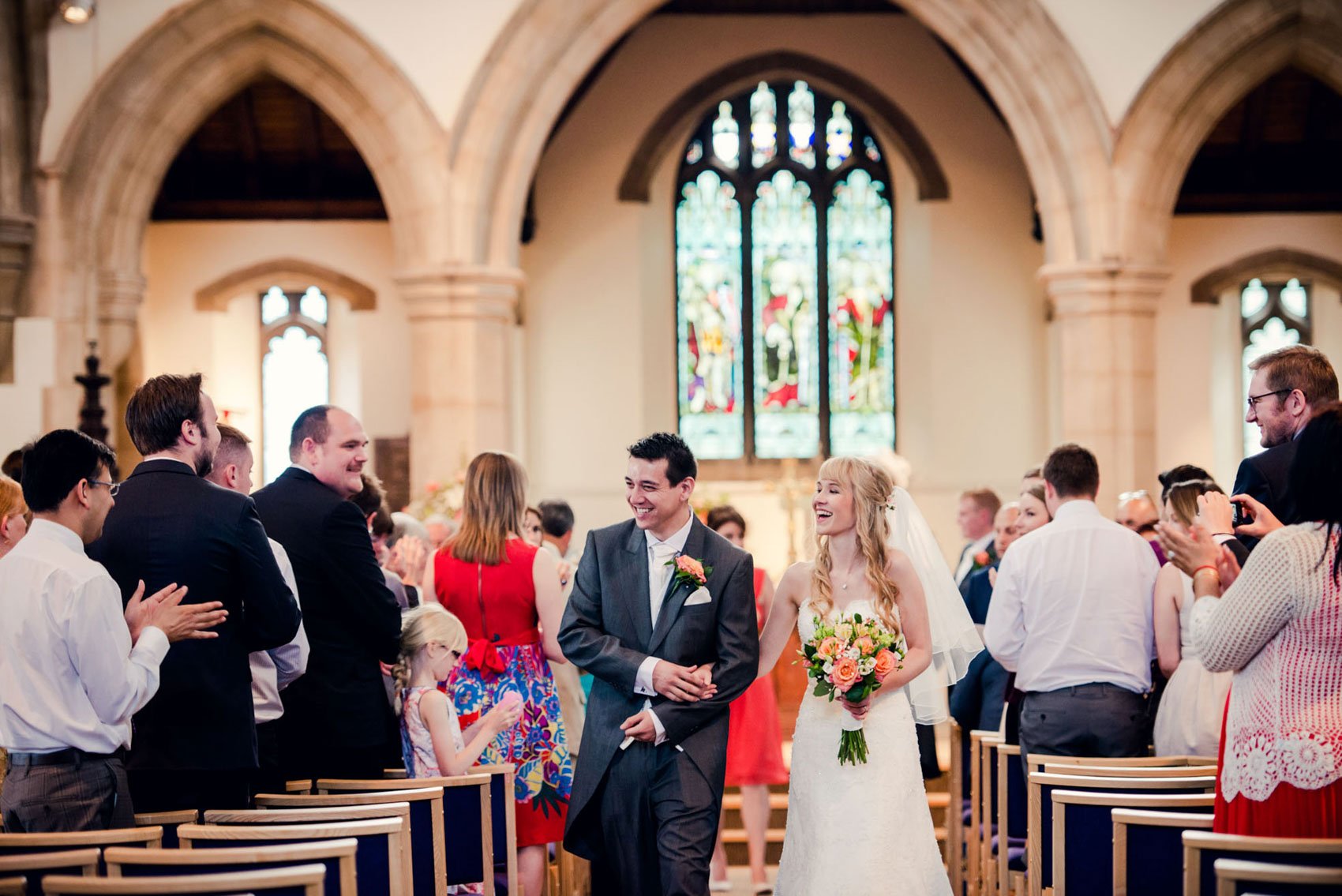 A bride and groom walk up the aisle together, laughing, following their church wedding in Bedfordshire