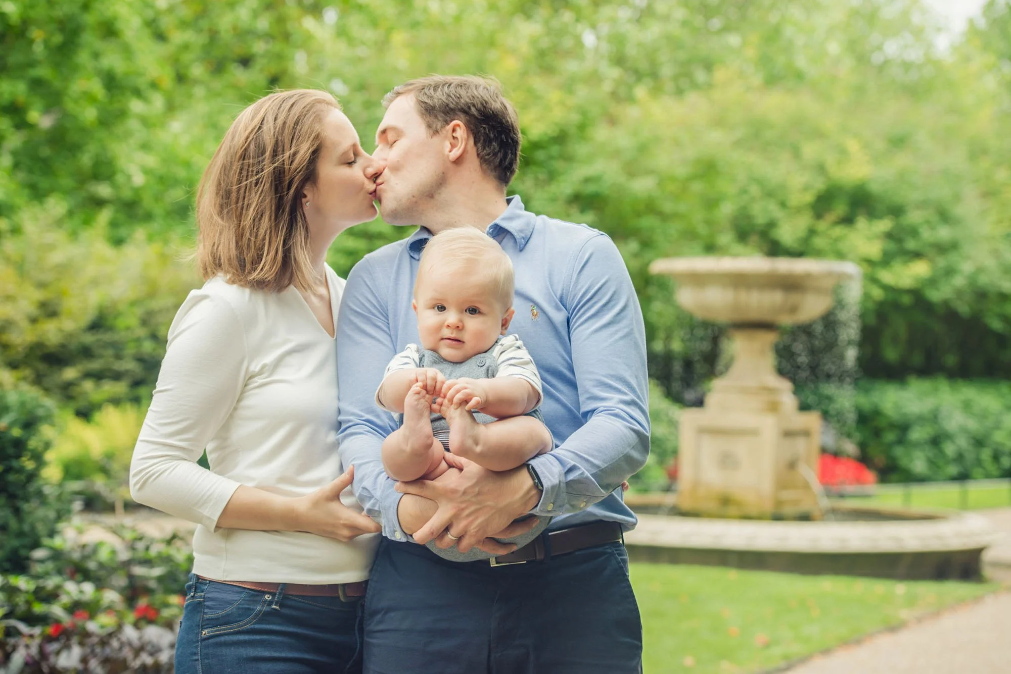 Parents kiss as the father holds their six month old baby in his arms in Regent's Park in London