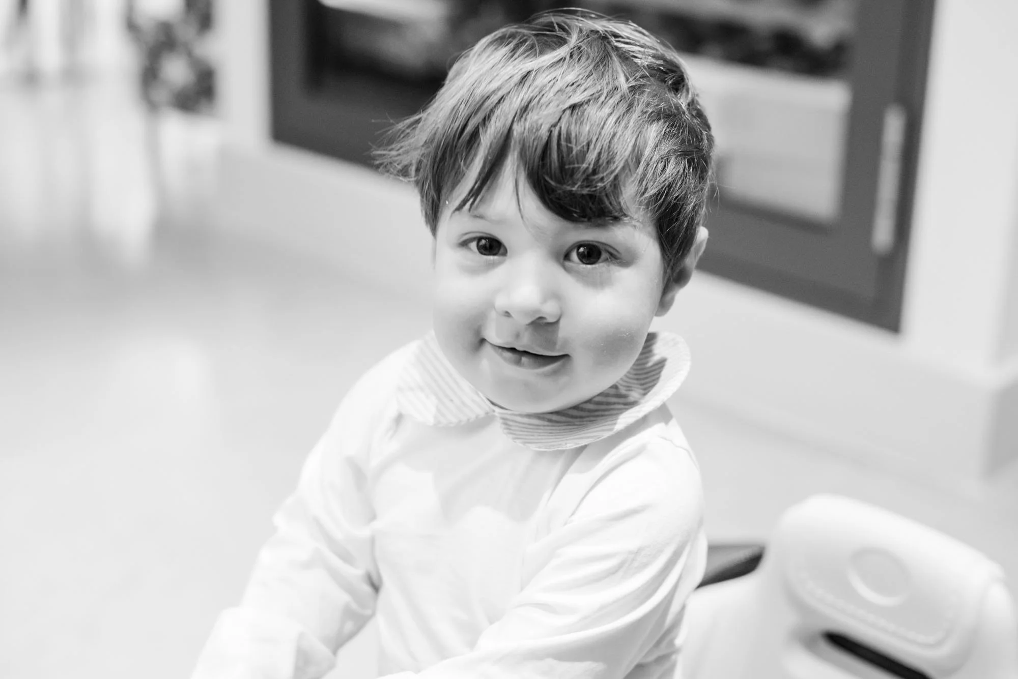 A black and white photo of a 1 year old boy sitting in his Hampstead home, smiling directly into the camera.