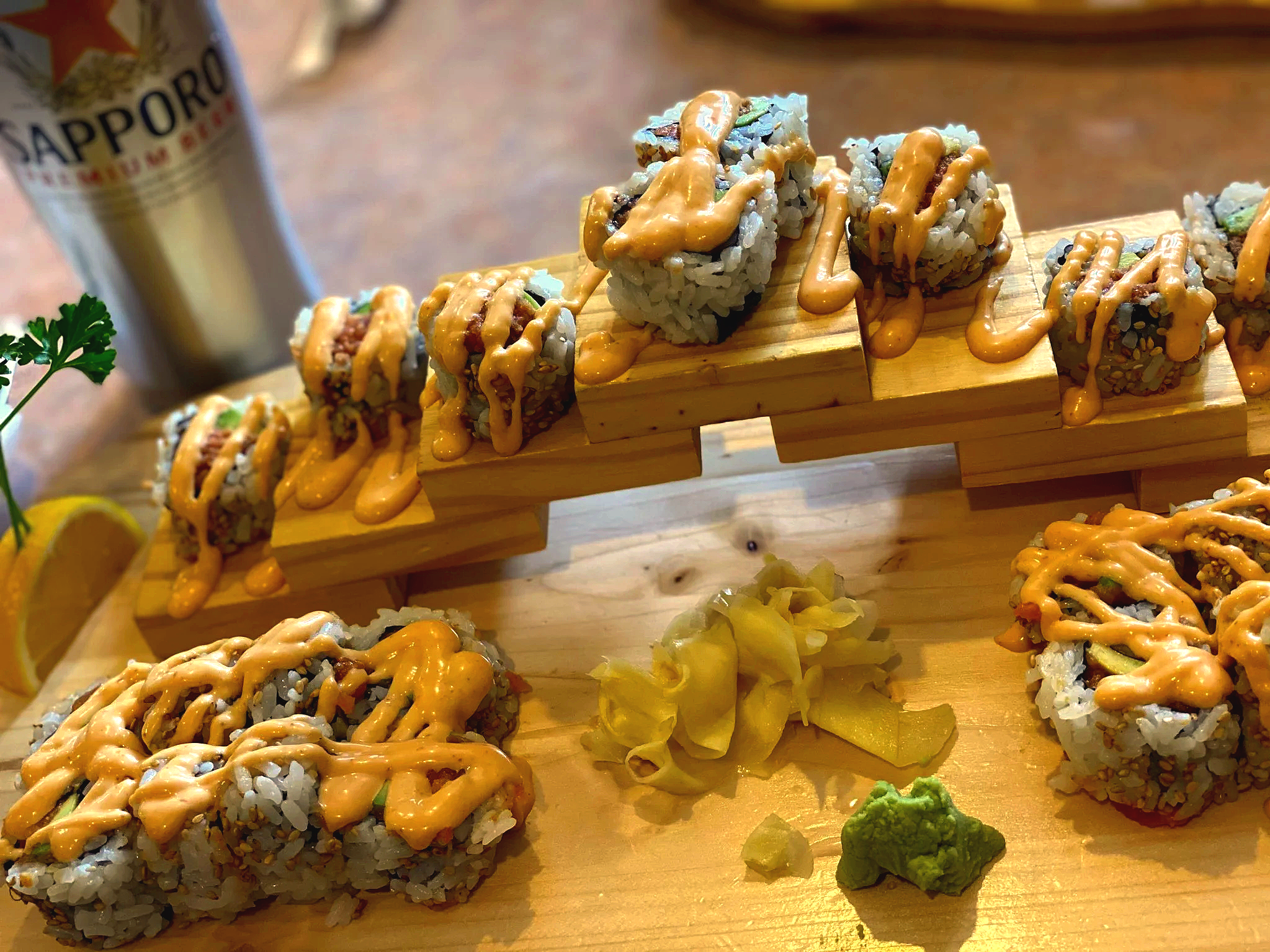 Sushi drizzled with sauce on plate with bright lighting and beverage with lemon garnish