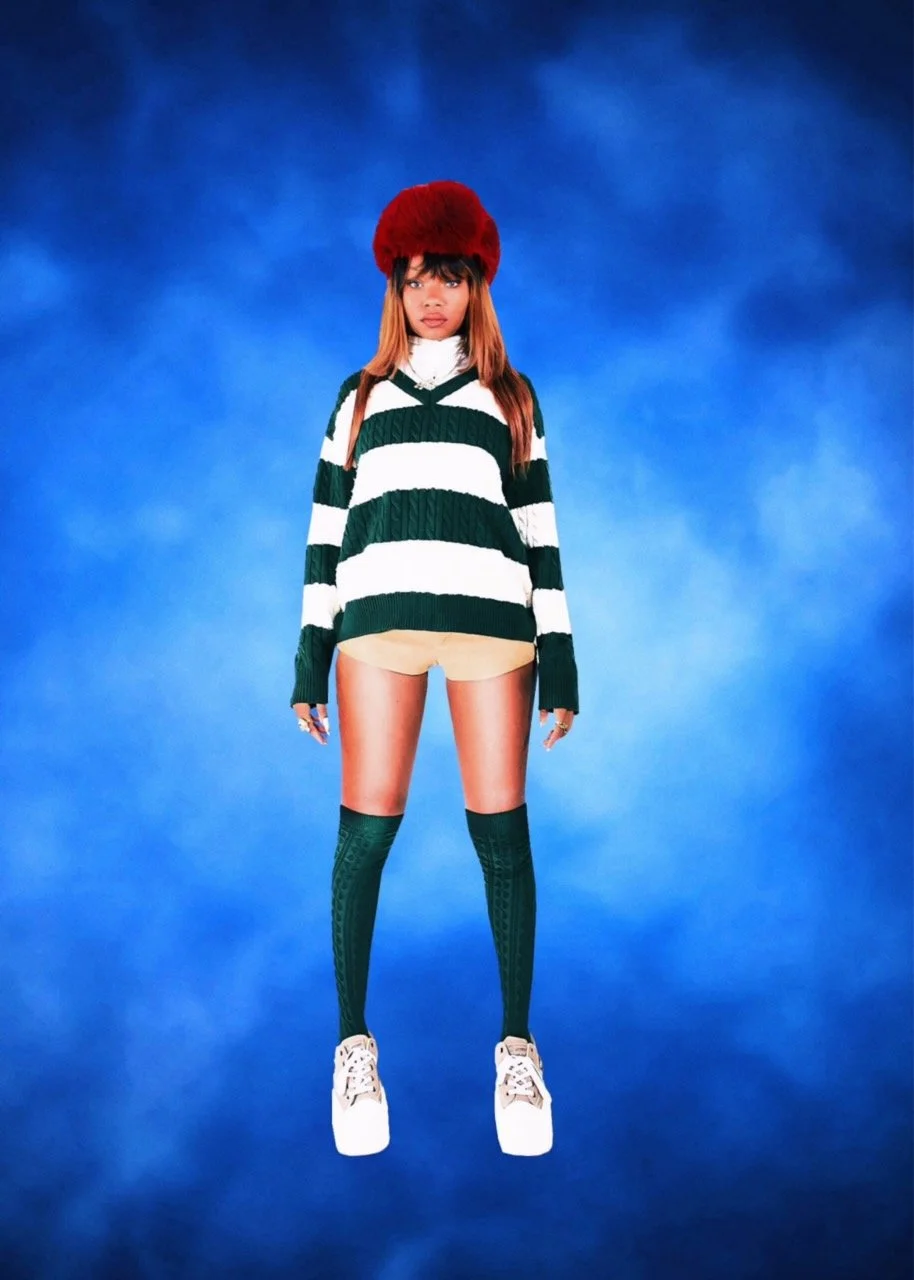 A young woman wearing a red fur hat, green and white striped sweater, beige shorts, green knee-high socks, and white sneakers, standing against a blue background.