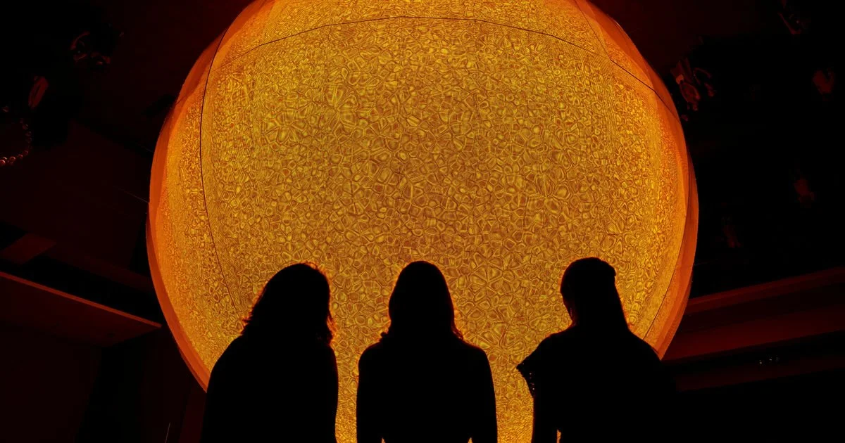 Three women silhouette with large orange hanging lantern with intricate patterns in the background.