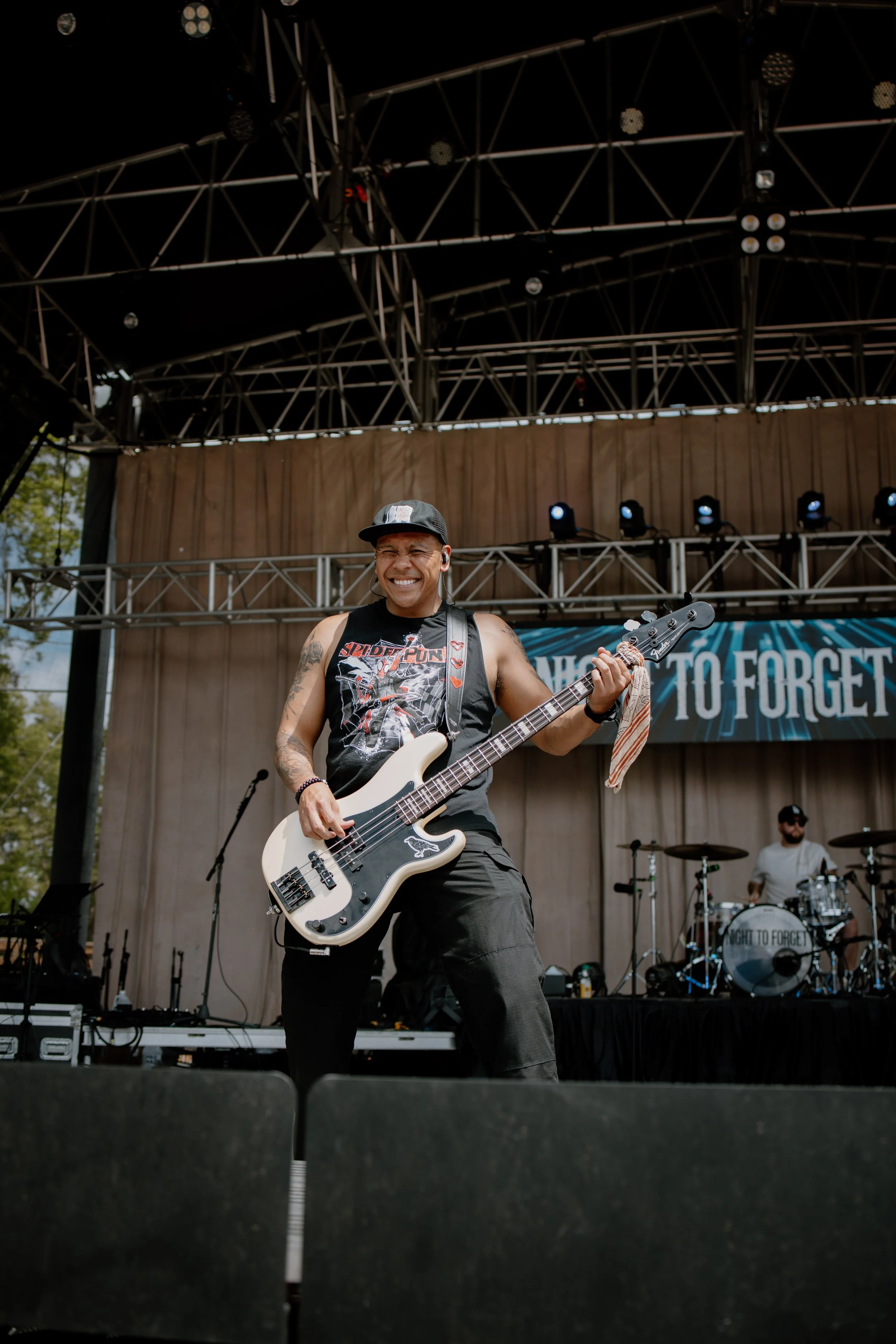 A male musician with tattoos playing a white bass guitar on stage at an outdoor concert.
