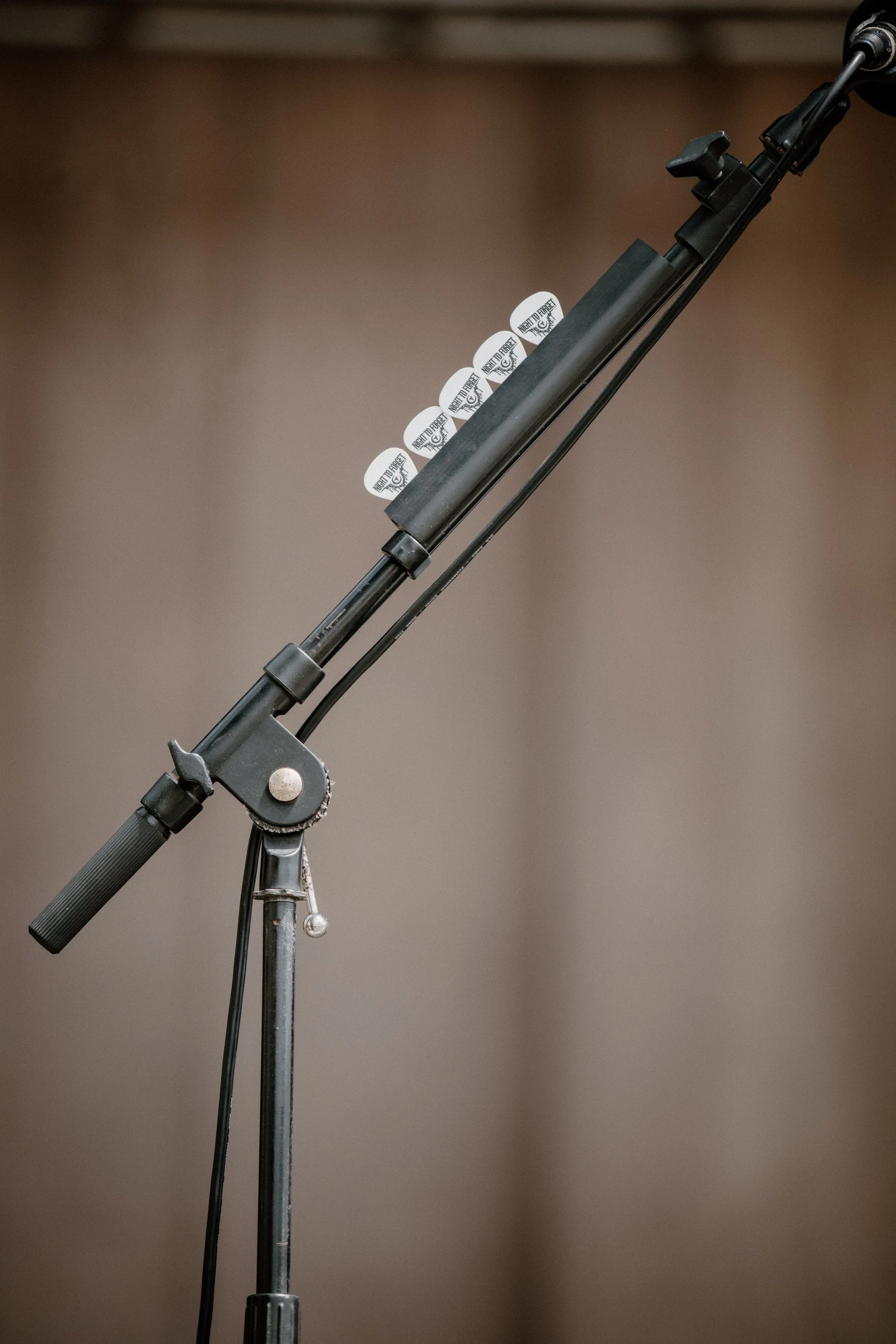 Microphone stand with six guitar picks attached, against a plain background.
