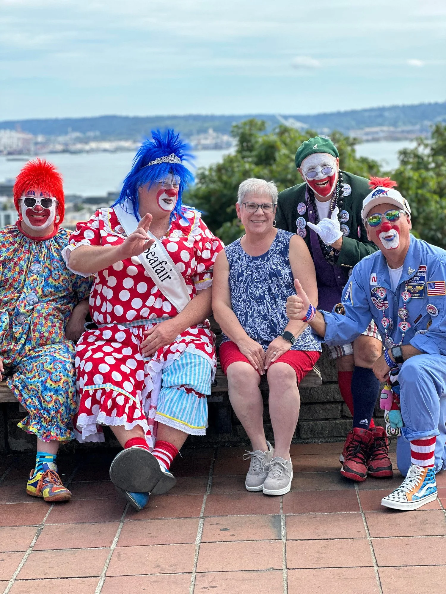 Susan Smith smiling with a group of colorful clowns during a fun outing overlooking the Seattle waterfront.