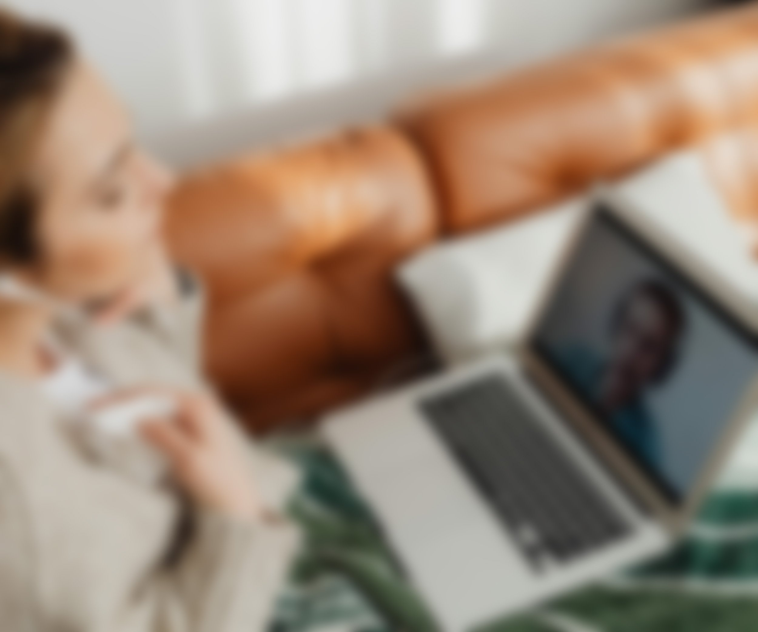 Woman participating in an online counseling or mentoring session from home while wrapped in a blanket on a couch.