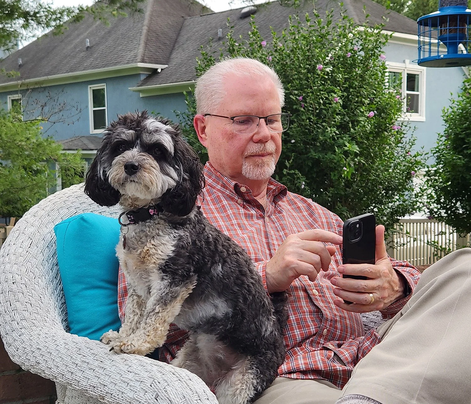 Kenny Smith sitting outdoors with one of the family dogs on his lap while relaxing on a backyard patio.