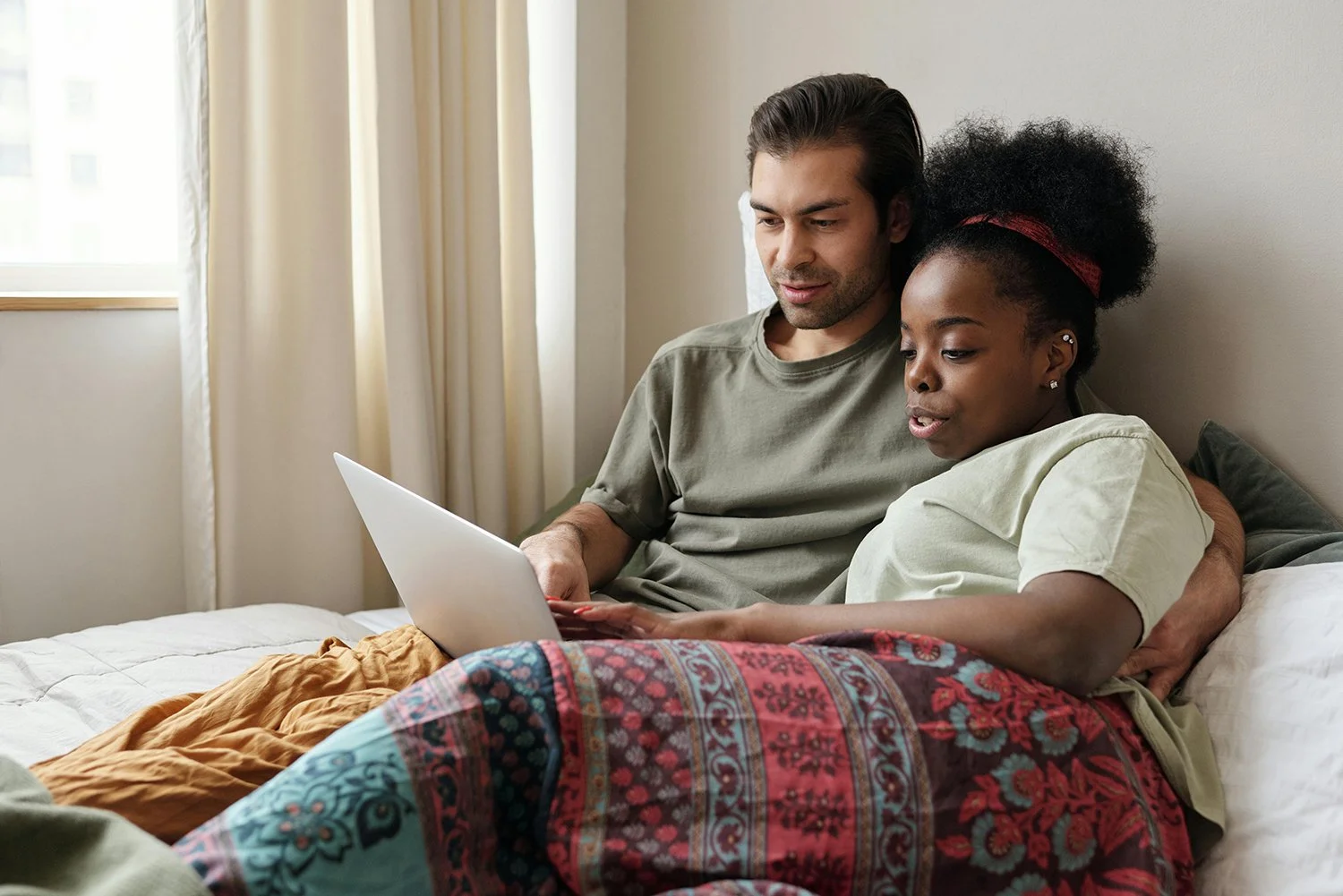 Couple sitting together on a bed while looking at online relationship or healing resources on a laptop.