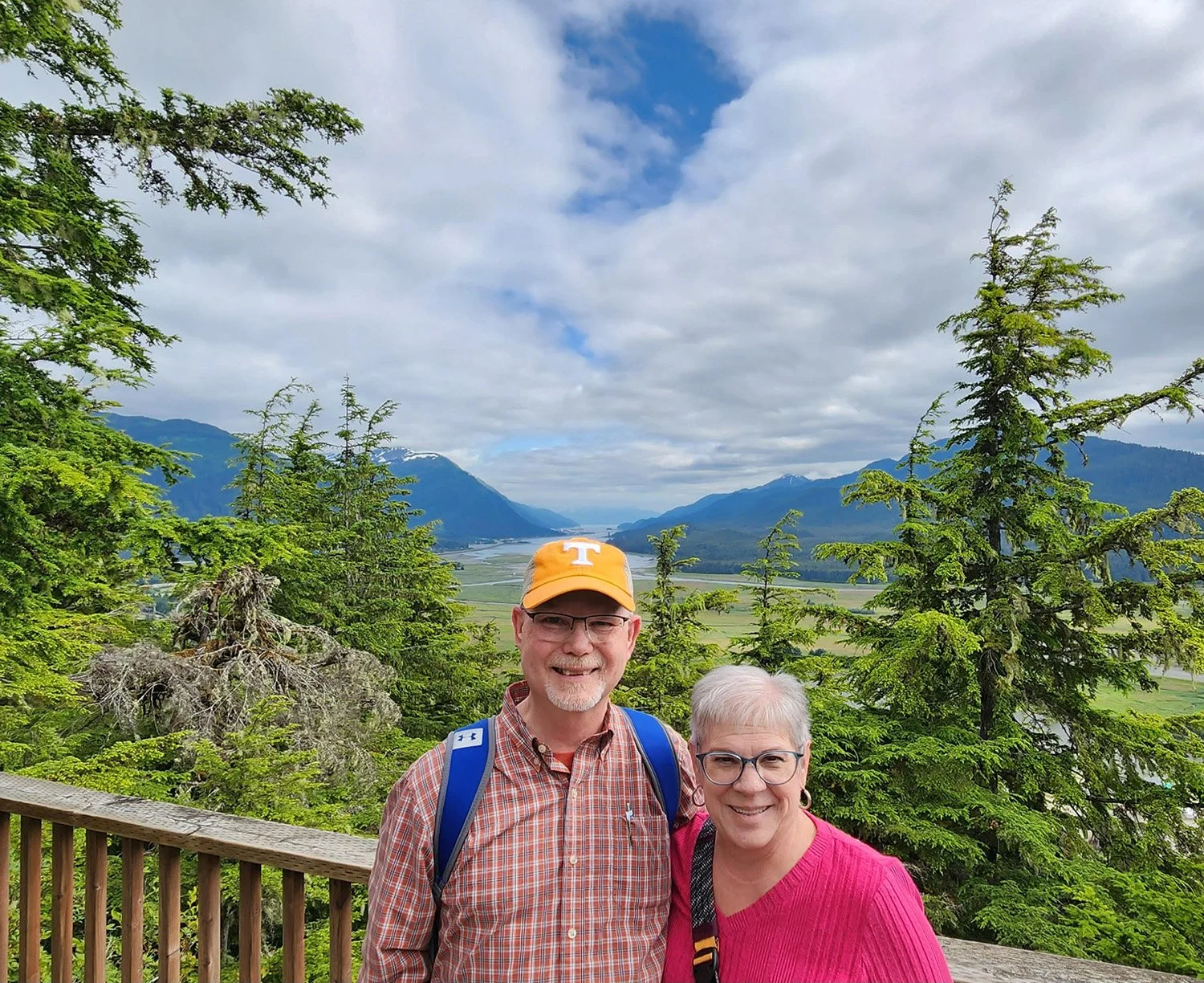 Kenny and Susan Smith smiling together at a scenic mountain overlook surrounded by trees and valleys during their travels.