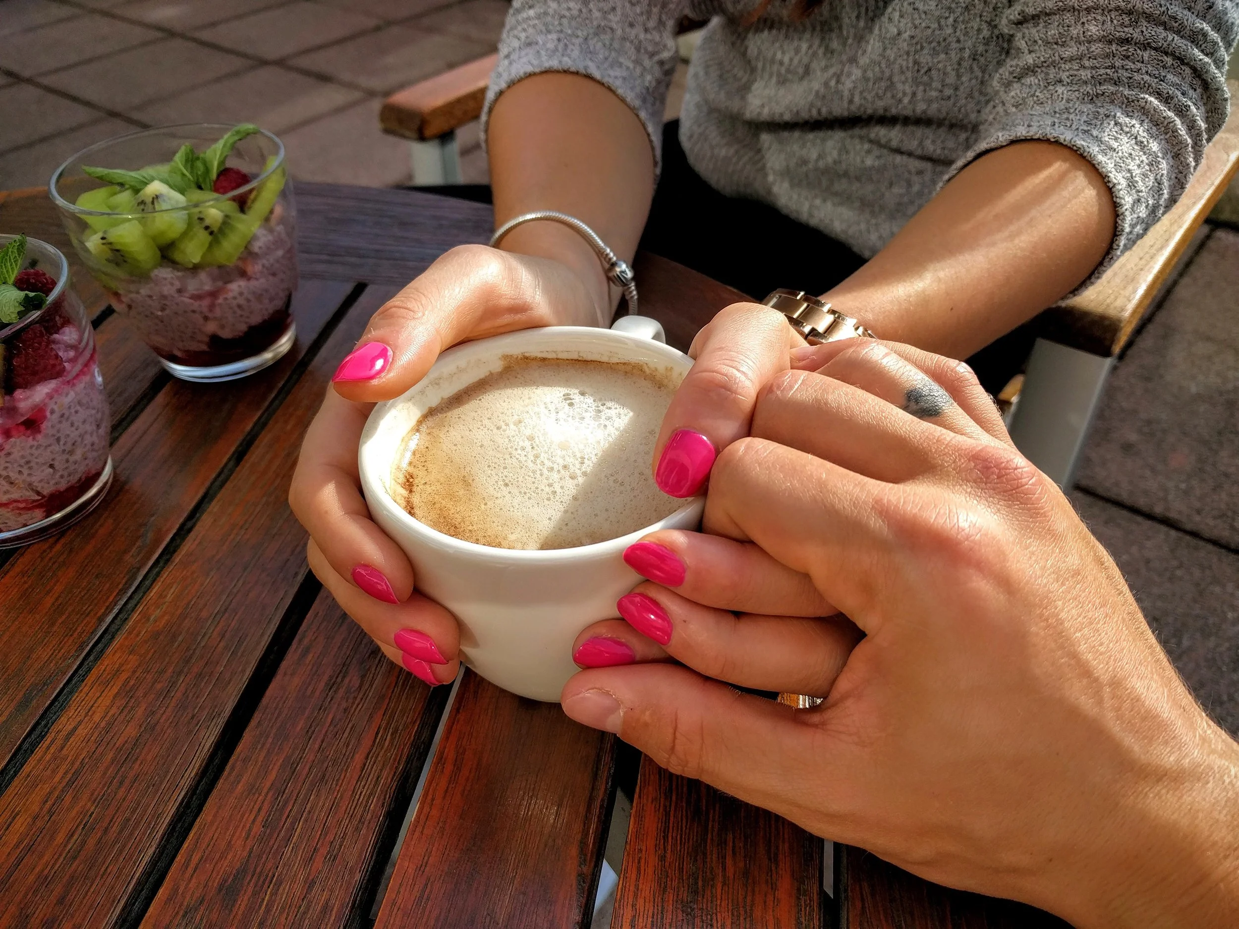 Two people holding hands around a cappuccino.