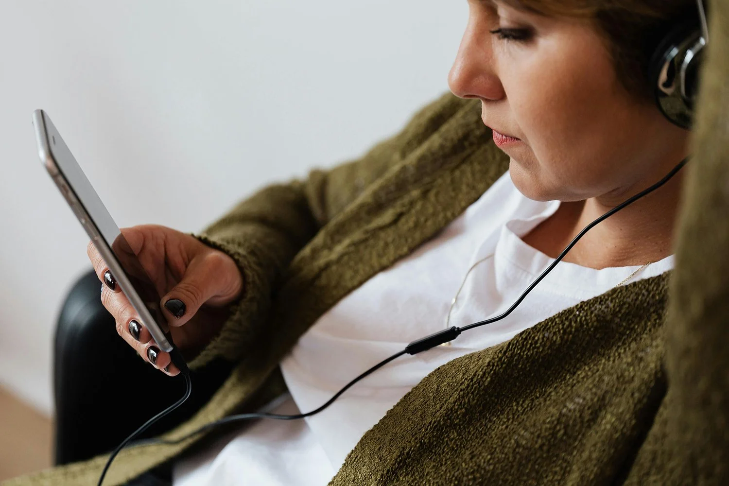 Woman listening to audio content or a healing podcast on her phone while relaxing with headphones on.