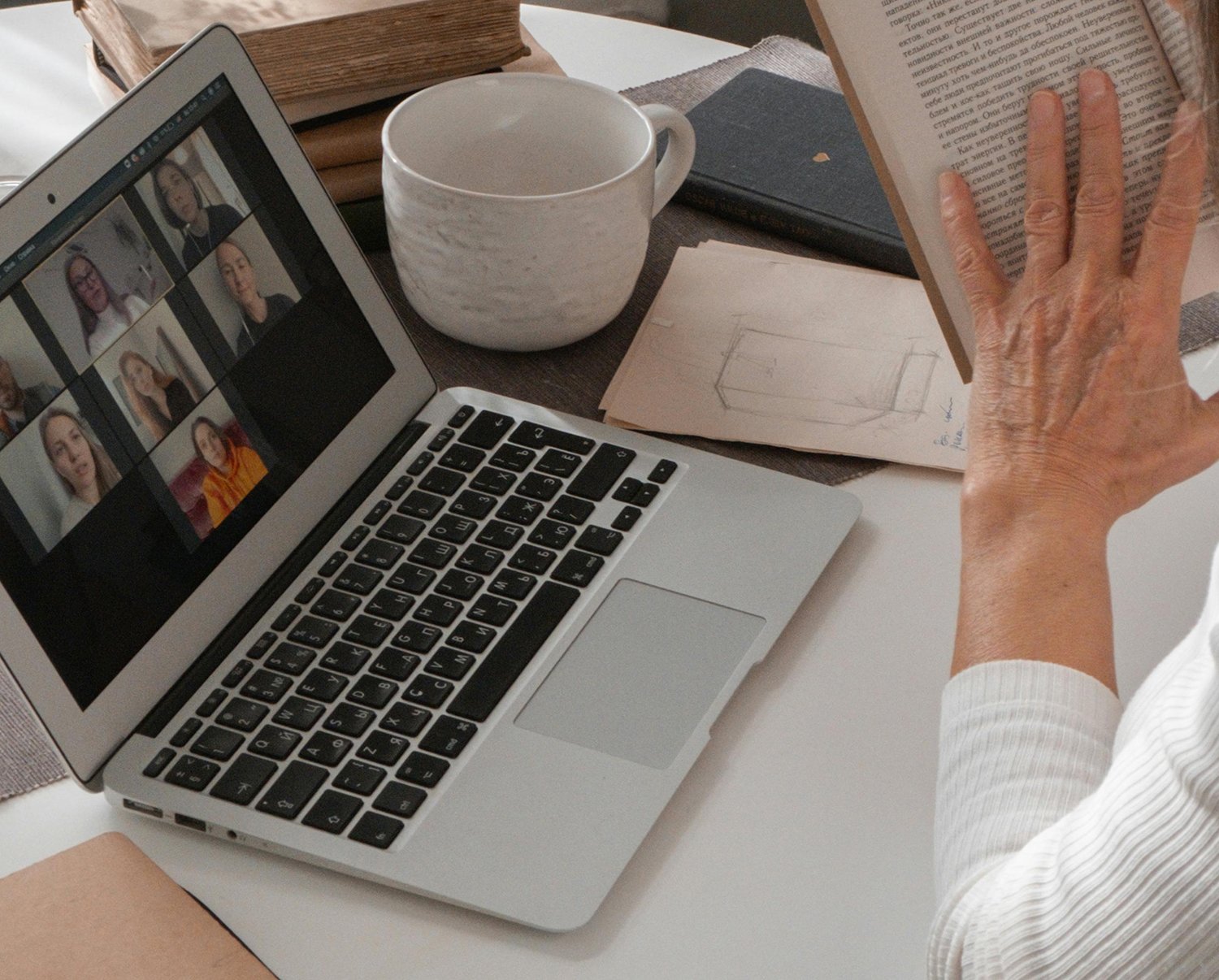 Person participating in an online group support or mentoring session while reading and taking notes at a desk.