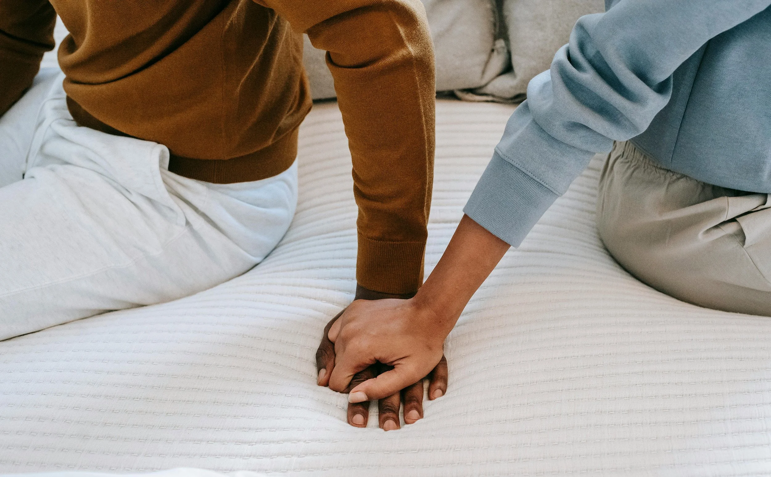 A couple sitting closely together holding hands, representing support, healing, and emotional connection.