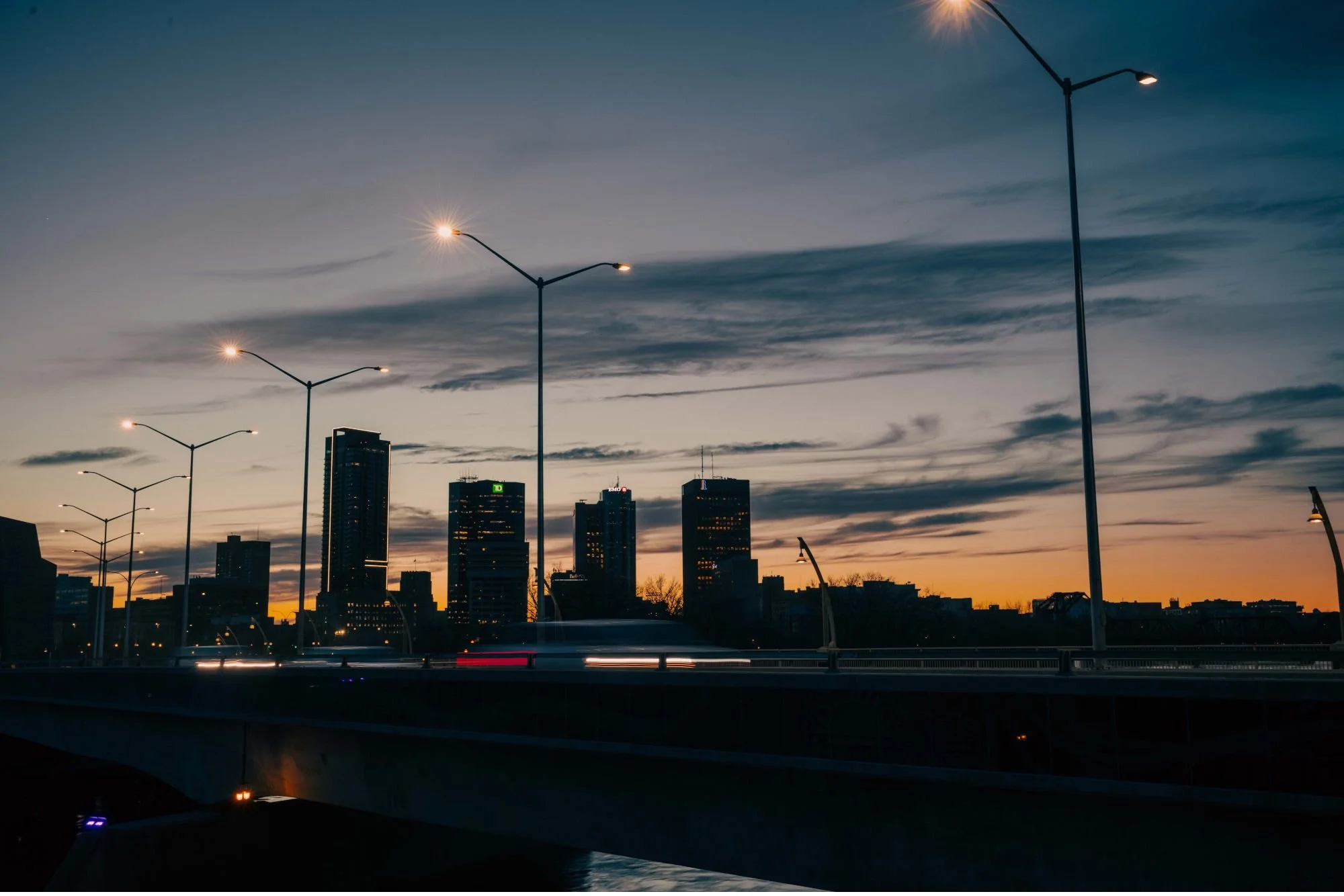City skyline at dusk with tall buildings and streetlights under a darkening sky.
