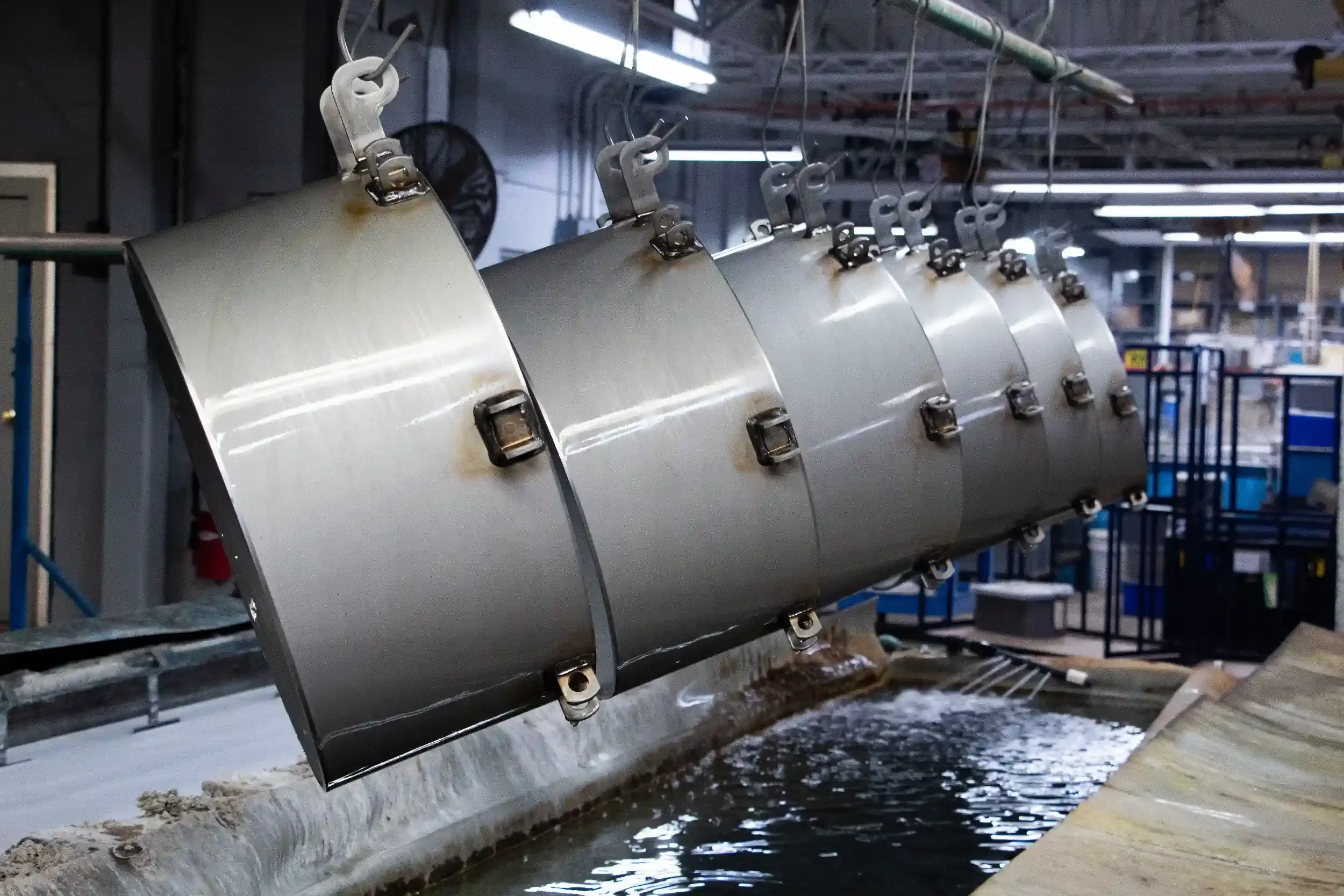 Multiple industrial metal components hanging above a water channel in an industrial setting.