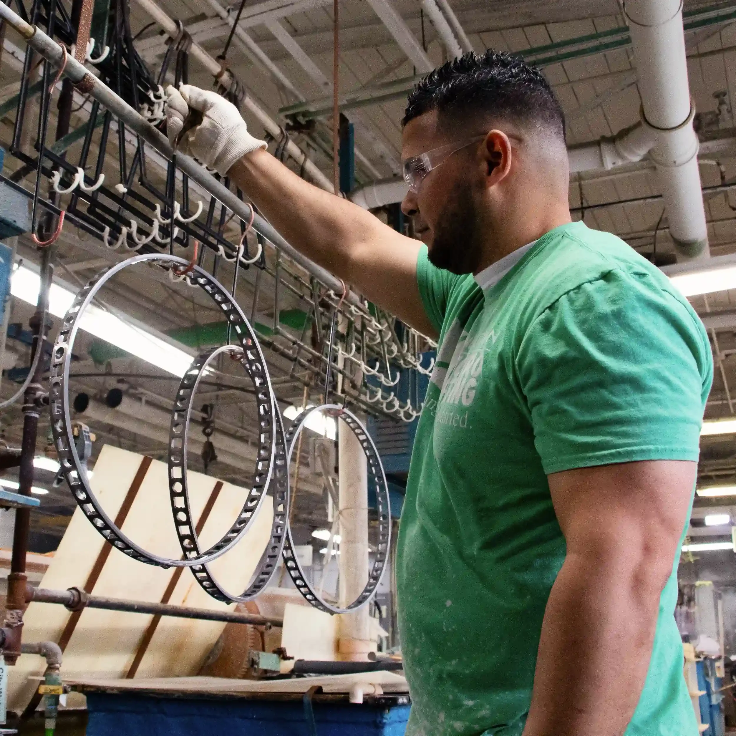 A man wearing glasses and a green shirt working with black and silver circular frames on a metal rack in an industrial setting.