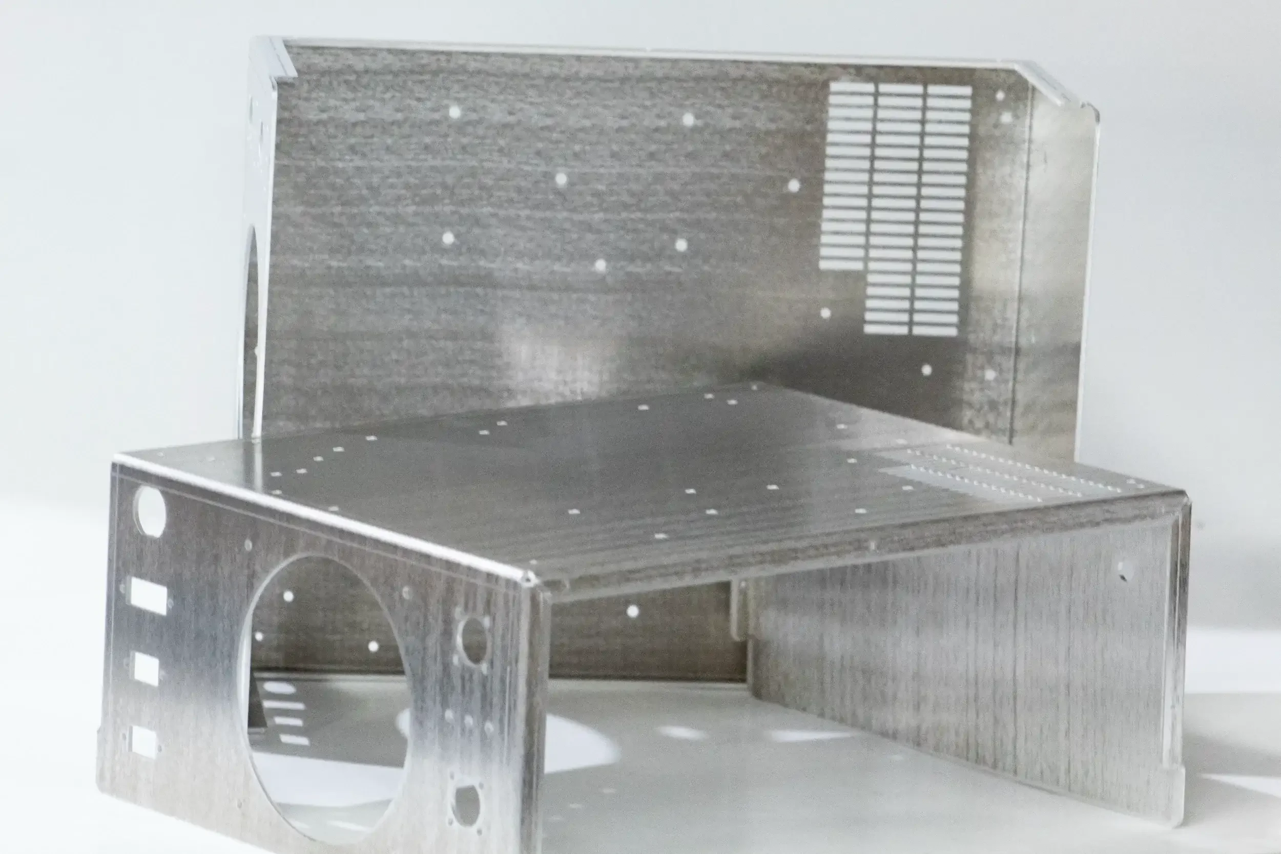 A small metallic structure with multiple circular and rectangular cutouts and a vent or grille on one side.