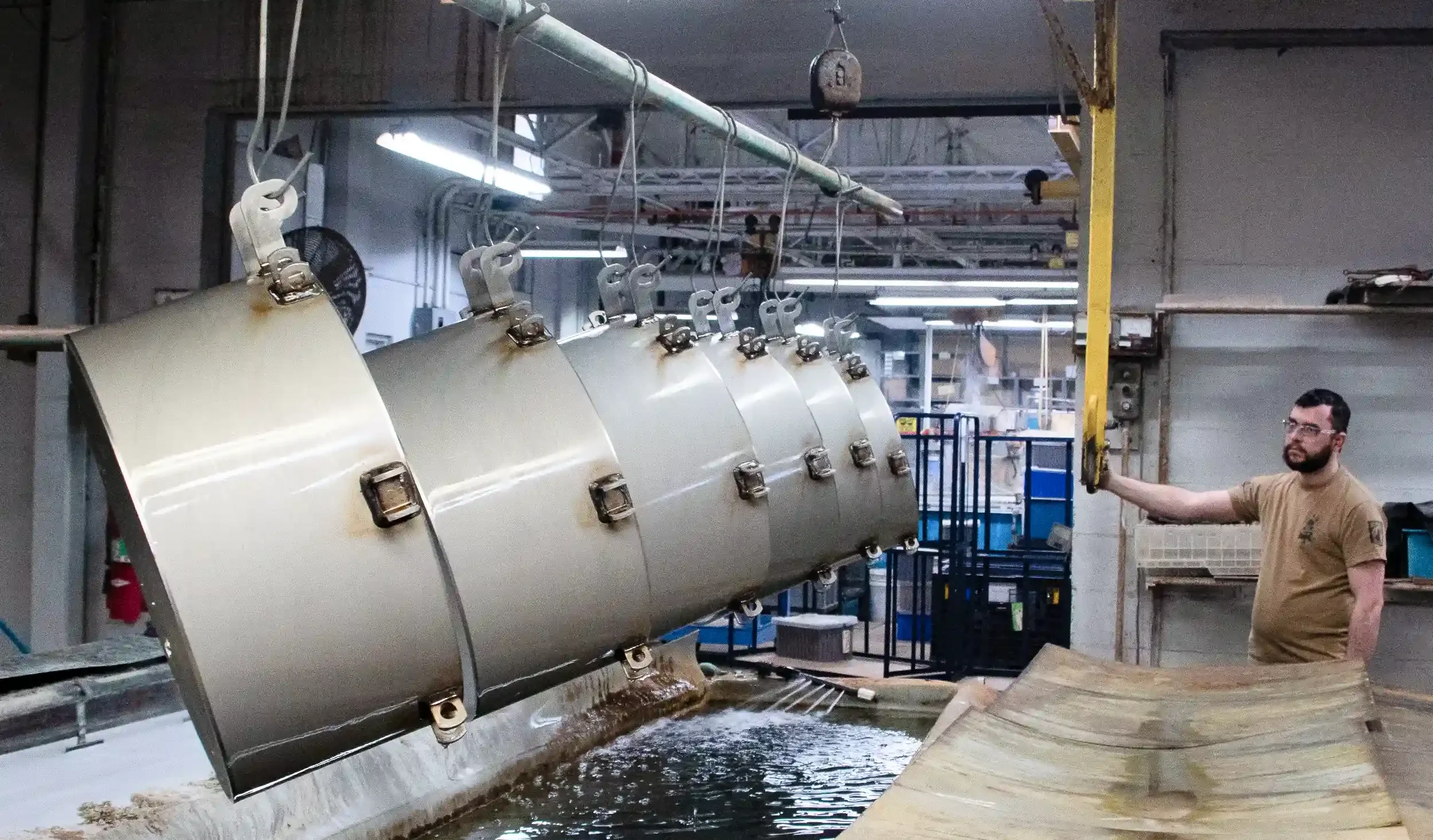 Worker standing next to and operating a large cylindrical industrial machine in a factory setting, with a platform and equipment in the background.