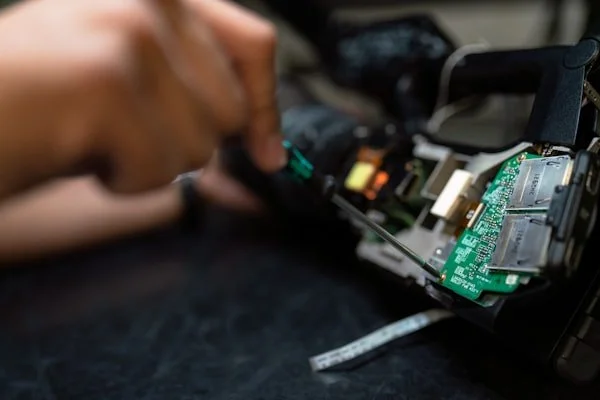 Close-up of a person's hand repairing or inspecting the circuit board inside an electronic device, possibly a smartphone or tablet.