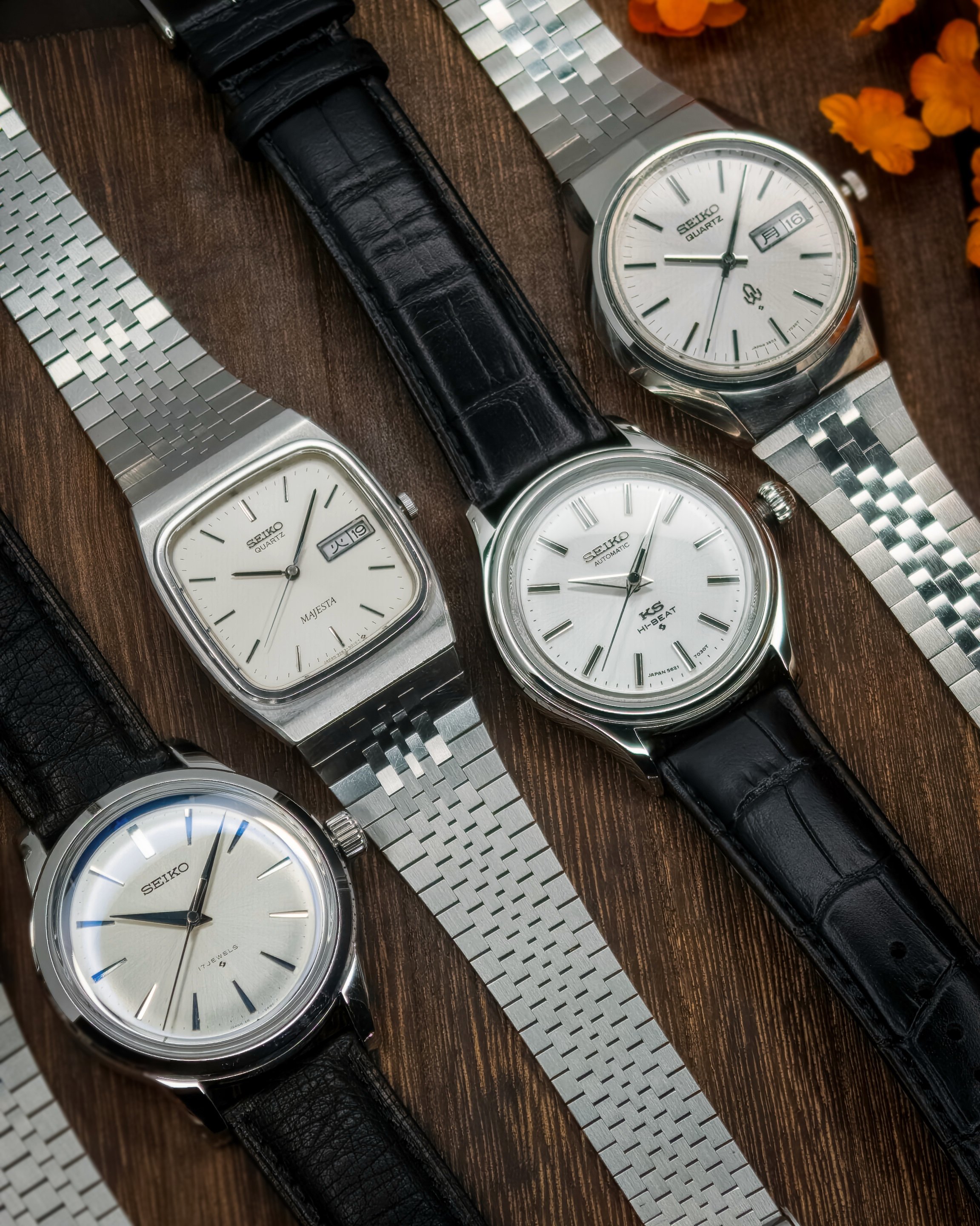 Fem vintage Seiko armbåndsur med ulike design, liggende på en mørk treflate med metallarmbånd og sort lærreim.