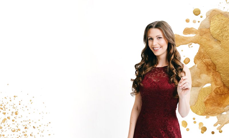 A young woman in a red lace dress smiling and pointing upward, with gold paint splashes in the background.