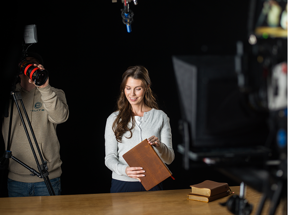 A woman smiling and holding a notebook in a studio with professional camera equipment around her.