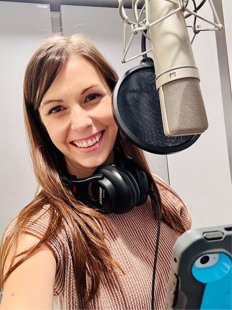 Young woman smiling in recording studio with microphone, headphones, and phone.