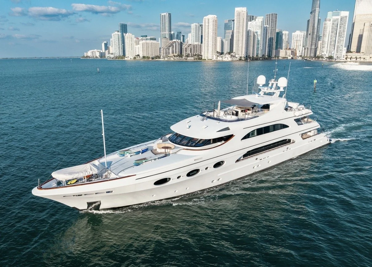 A large white luxury yacht sailing in the water near a city skyline with tall buildings in the background.